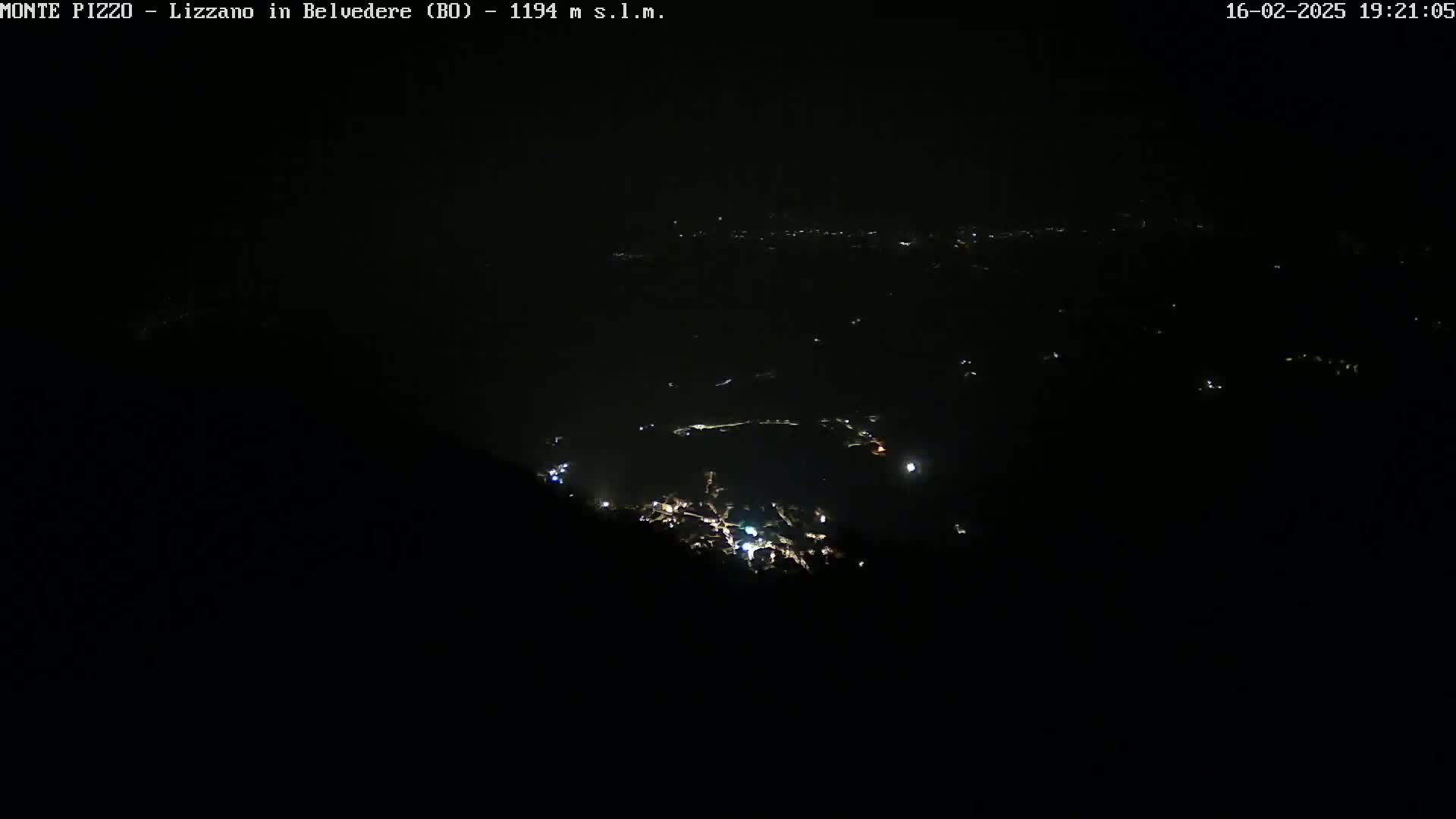 A nighttime, long-range view of a valley with scattered lights below, under a clear, dark sky.