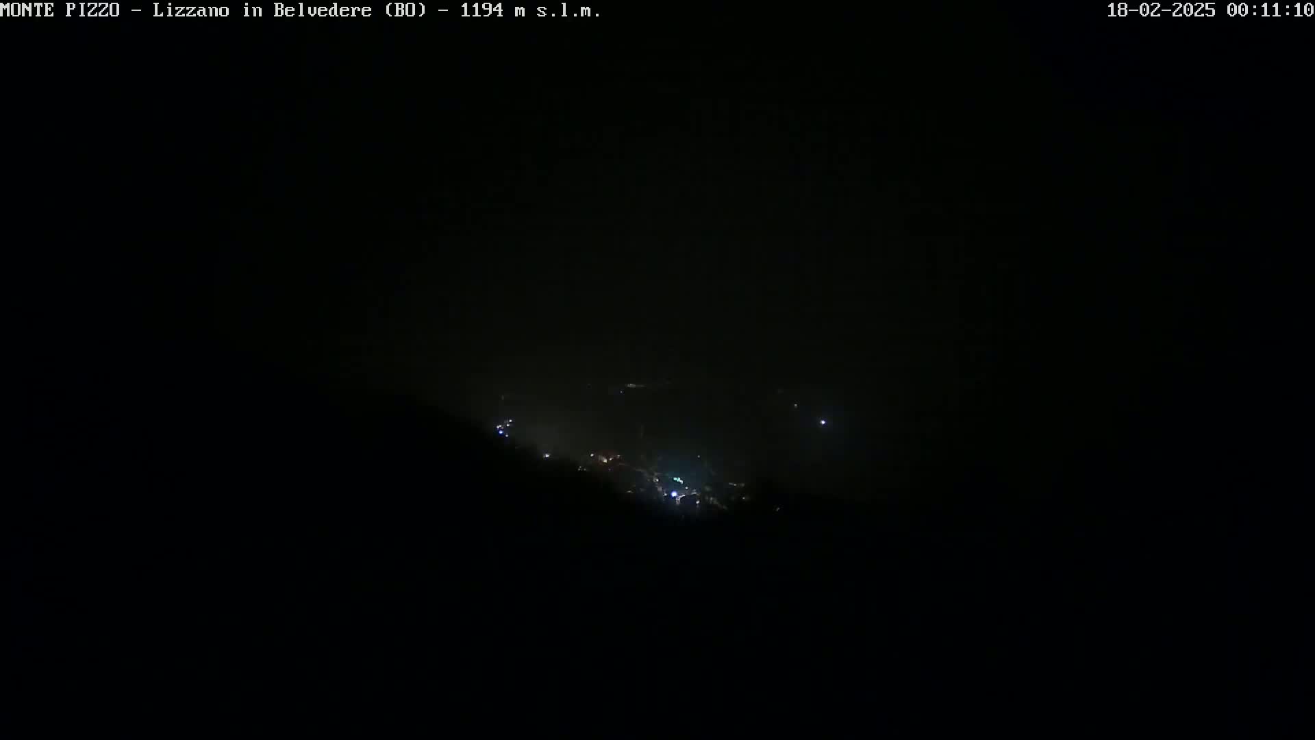 A dark, nighttime view shows a few faint lights in the distance, possibly a town, partially obscured by fog or haze.