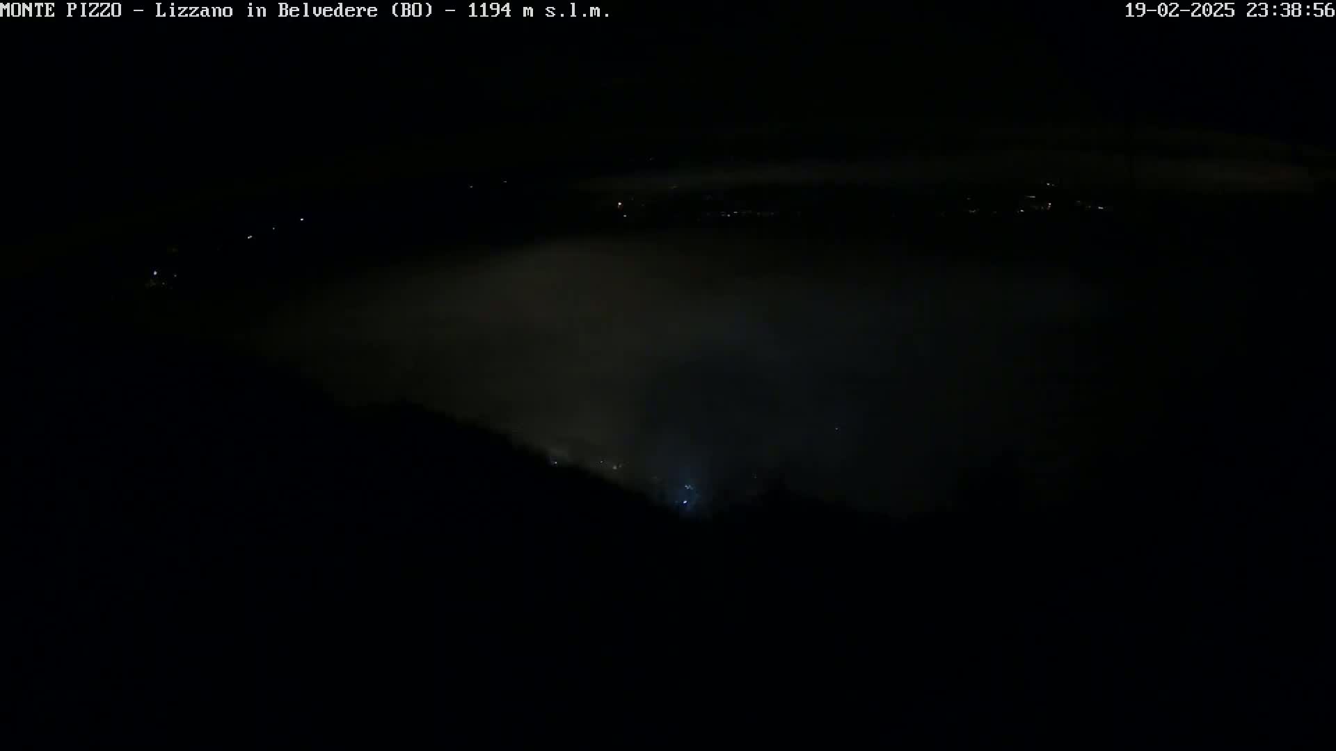 A nighttime, foggy view shows a dark landscape with a few distant lights.