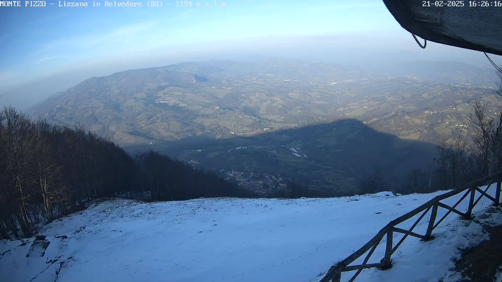 A snow-covered hillside overlooks a vast valley under a clear blue sky.