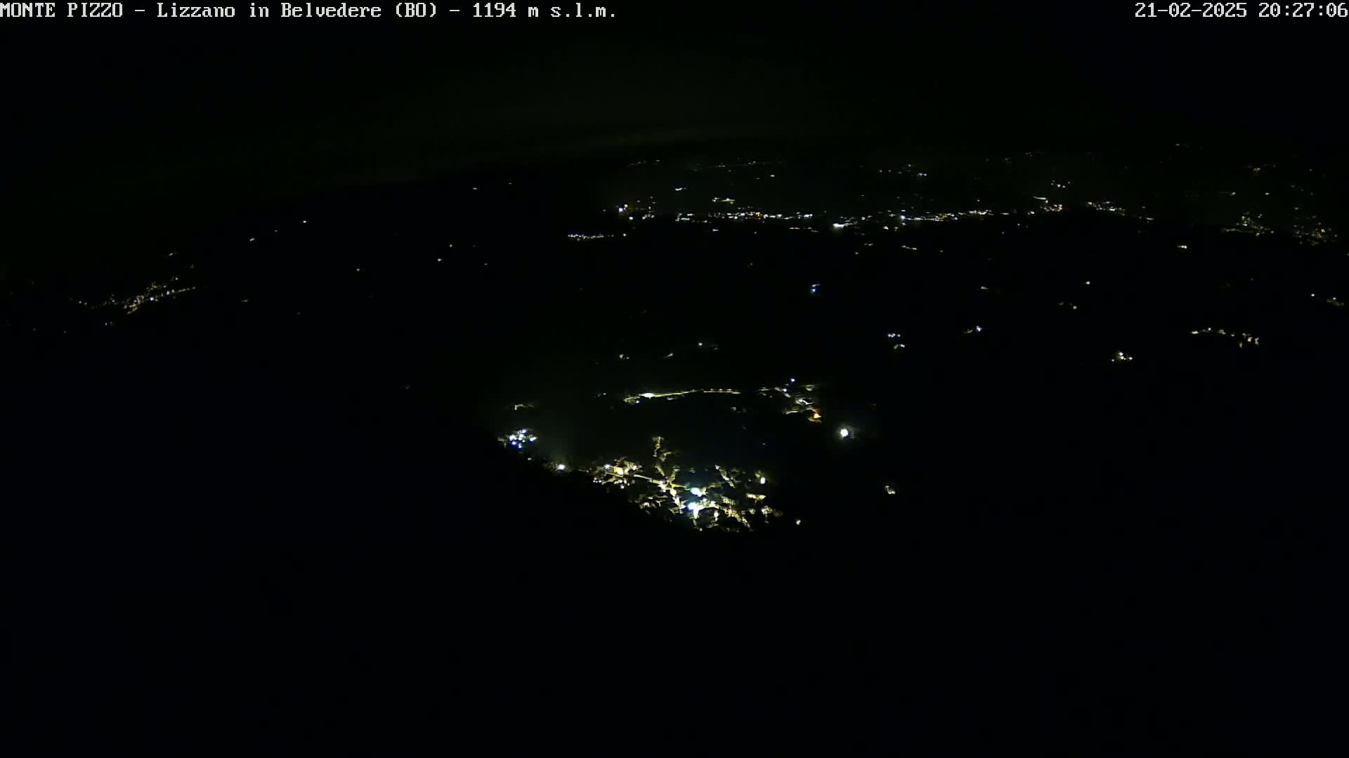 A nighttime, high-angle view shows a sparsely lit town nestled in a dark landscape.