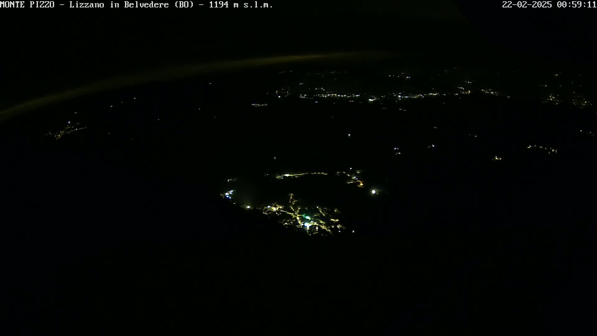 A nighttime aerial view shows a dark landscape with scattered lights from a town below.