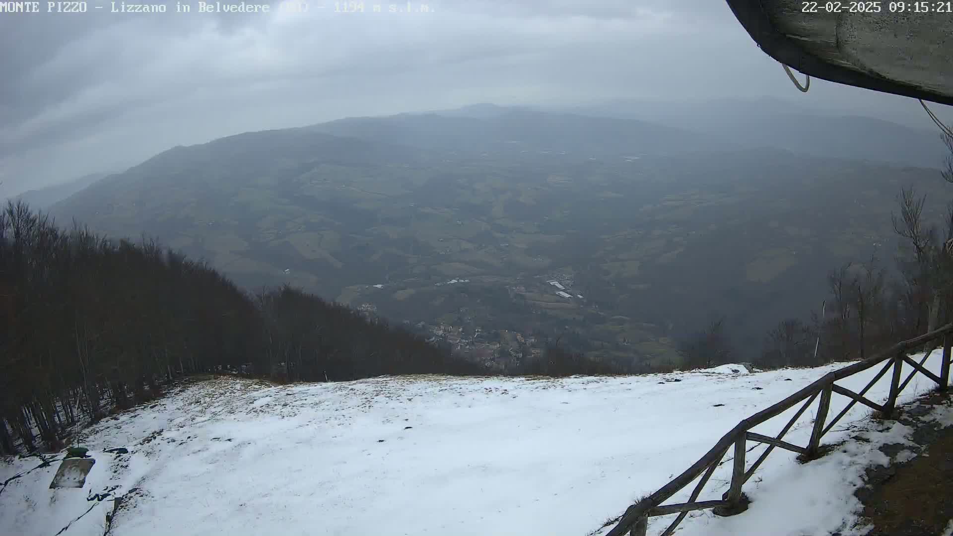 A snow-covered hilltop overlooking a valley under an overcast sky.