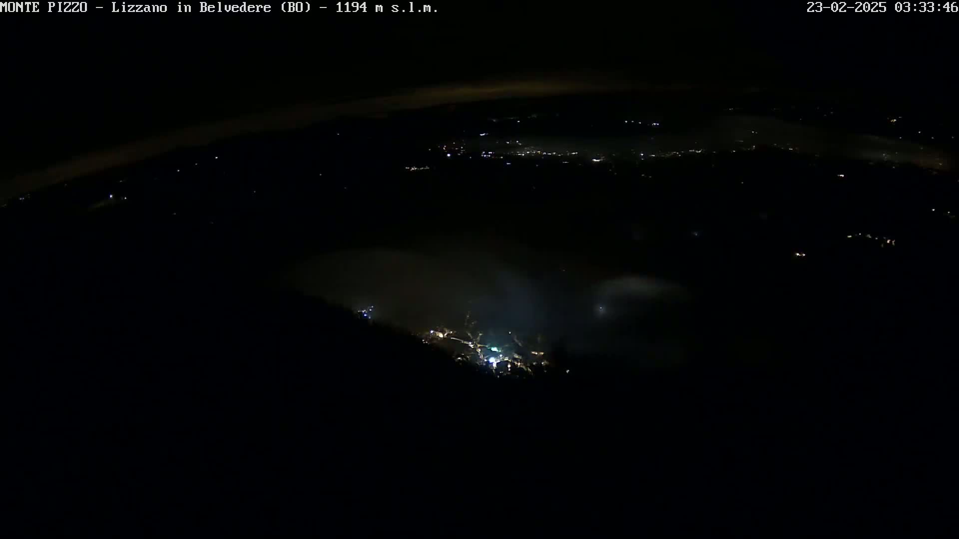 A nighttime, high-angle view shows a valley shrouded in fog with scattered lights visible below.