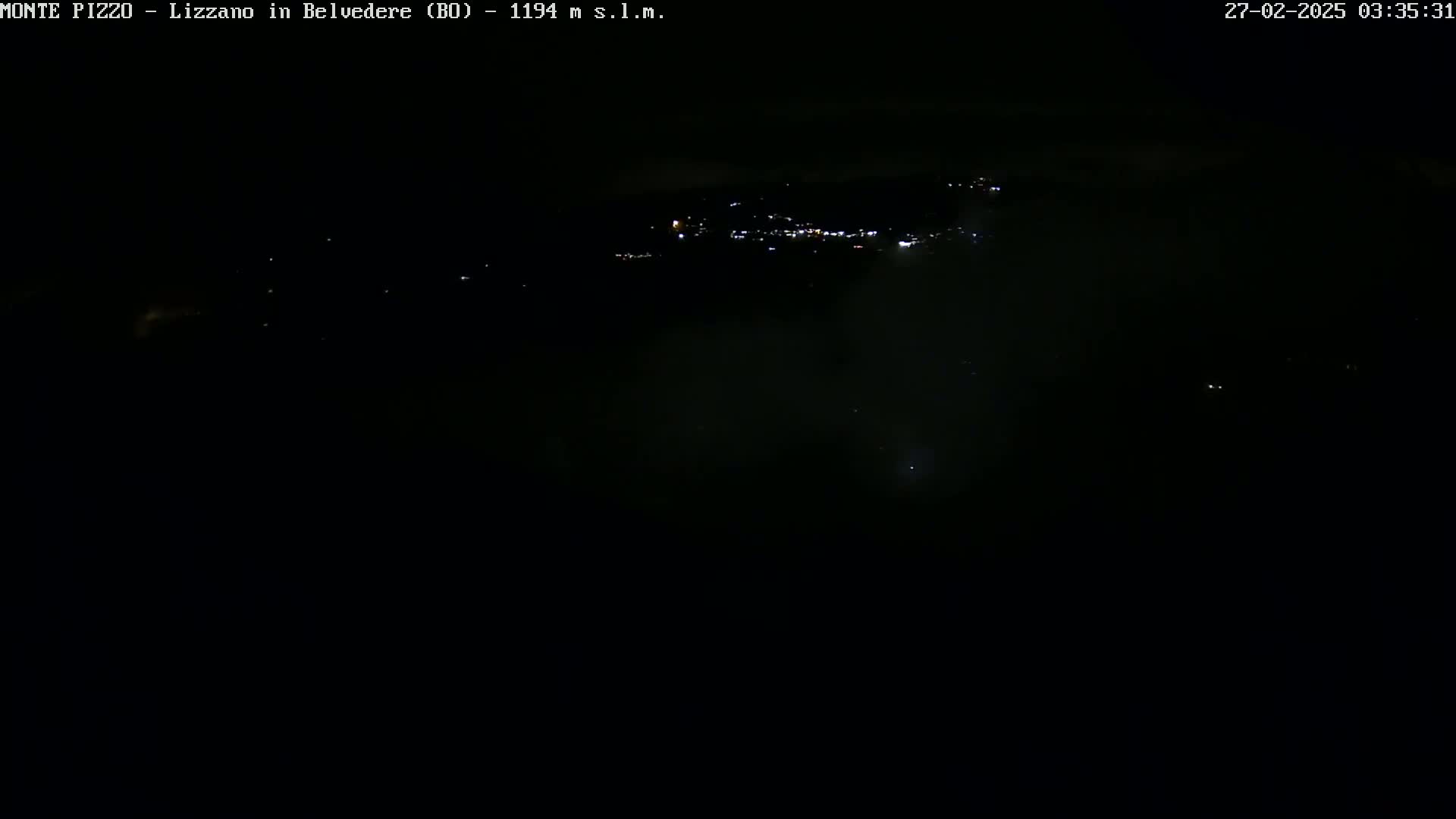 A nighttime long shot shows a distant town with faint lights, partially obscured by darkness and a possible fog or haze.