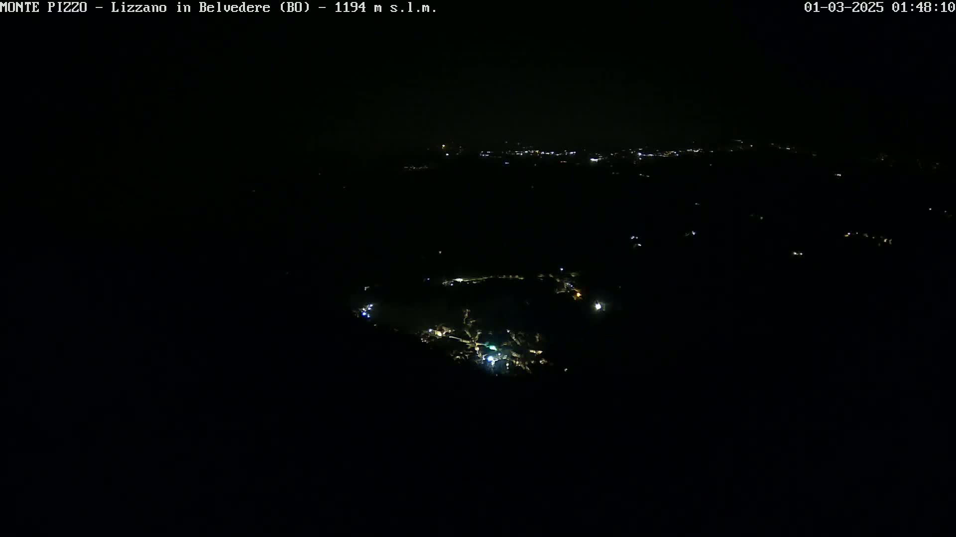 A nighttime, high-angle view shows a small town illuminated by scattered lights against a completely dark sky.