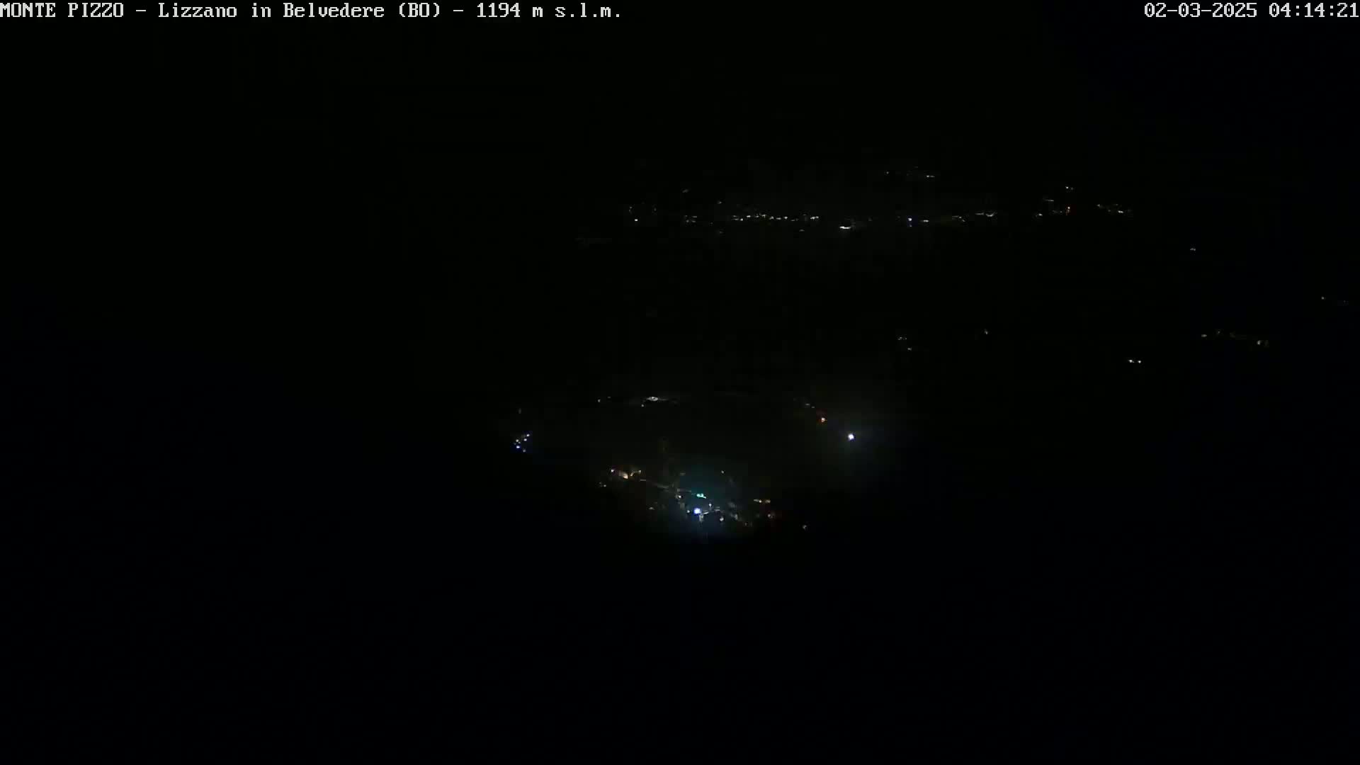 A dark, nighttime view shows a sparsely lit landscape with a few scattered lights visible in the distance.