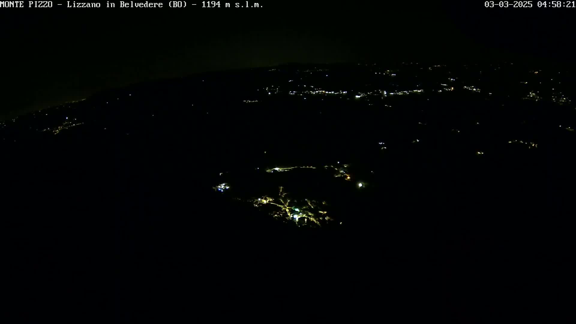 A nighttime, high-angle view shows a dark landscape sparsely dotted with small, faint lights.