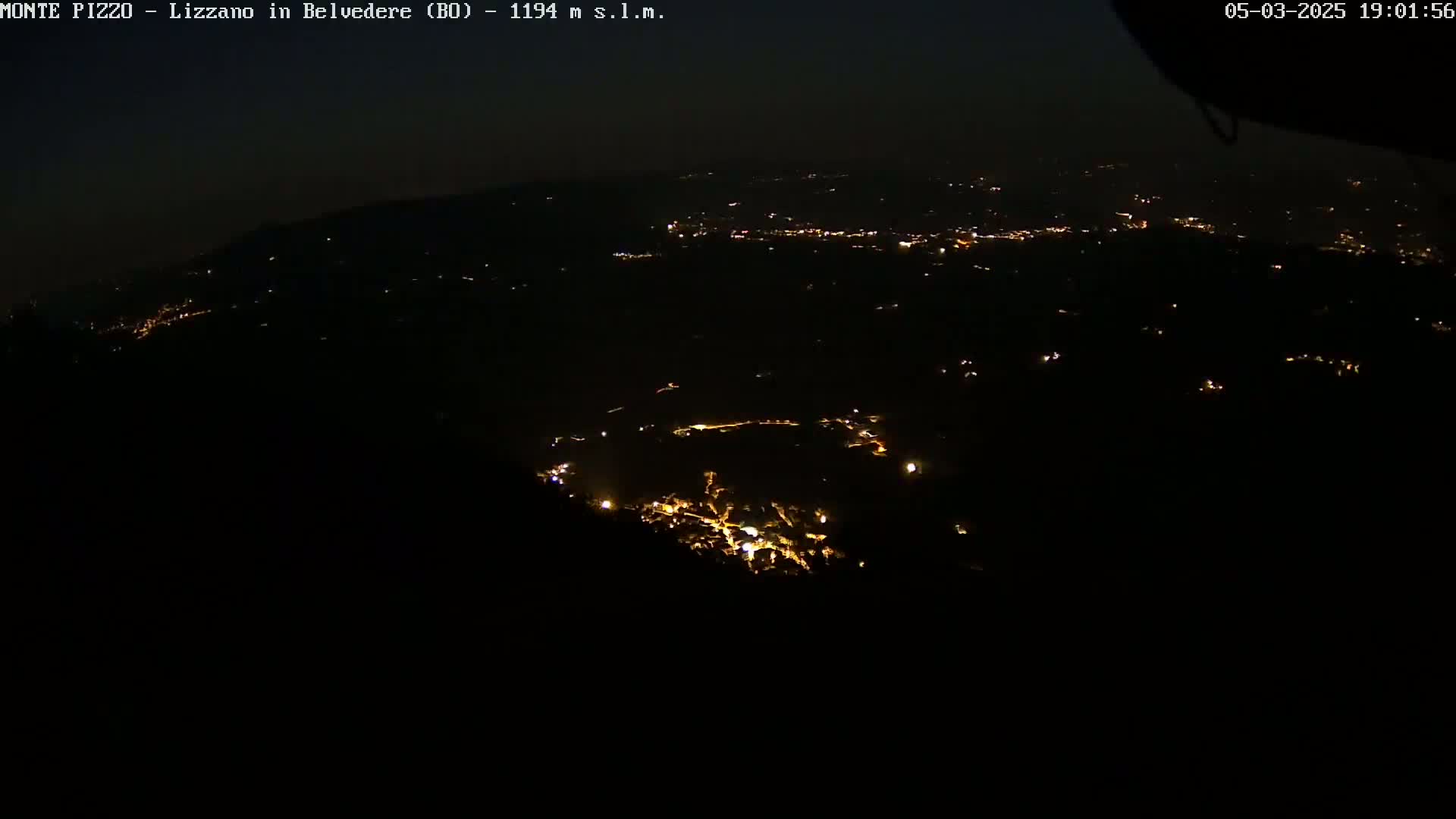 A nighttime, high-angle view shows a sprawling landscape dotted with sparsely scattered lights, likely a town or village, under a dark sky.