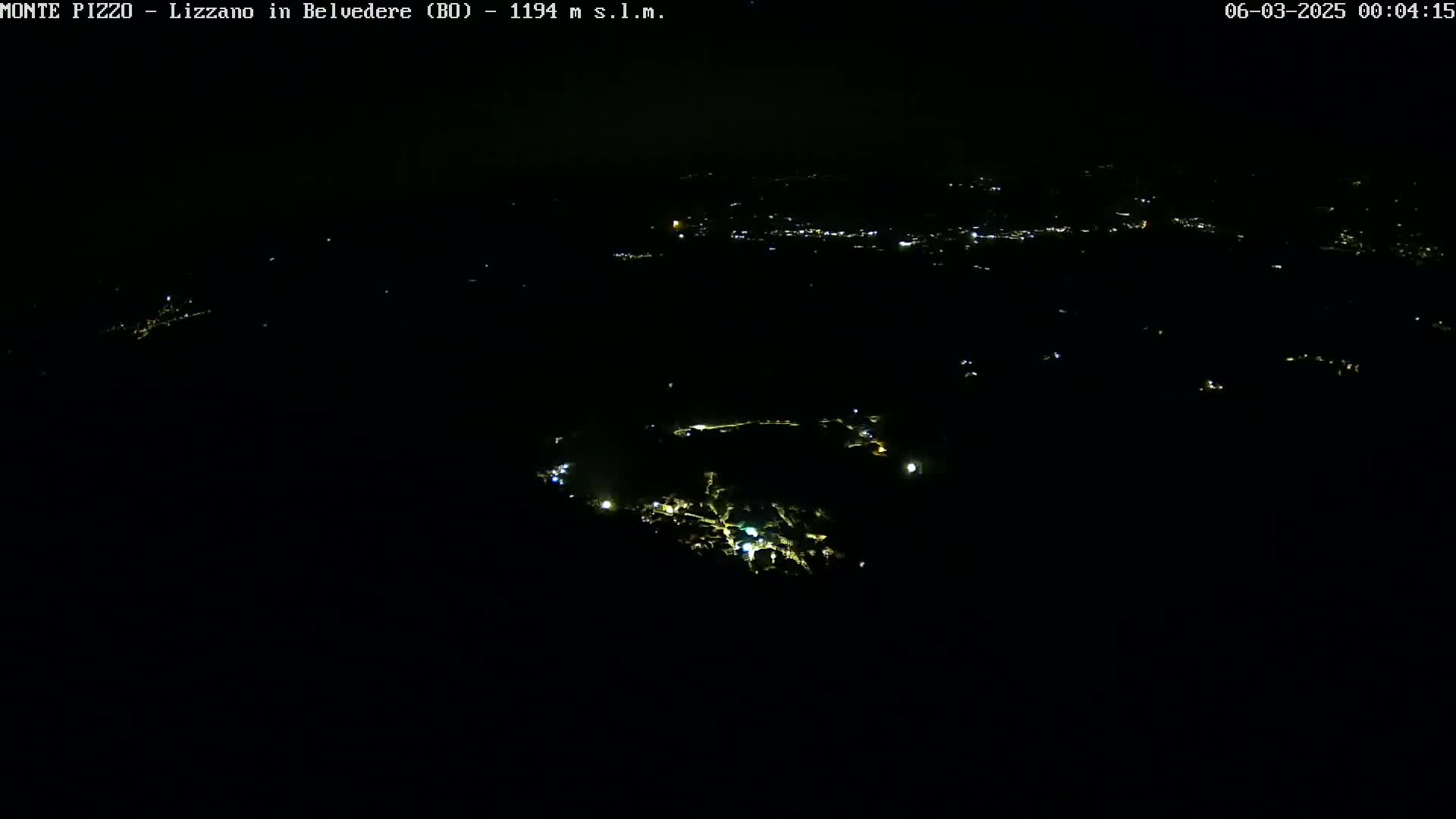 A nighttime, high-angle view shows a scattering of small, distant lights in a dark, mountainous landscape.