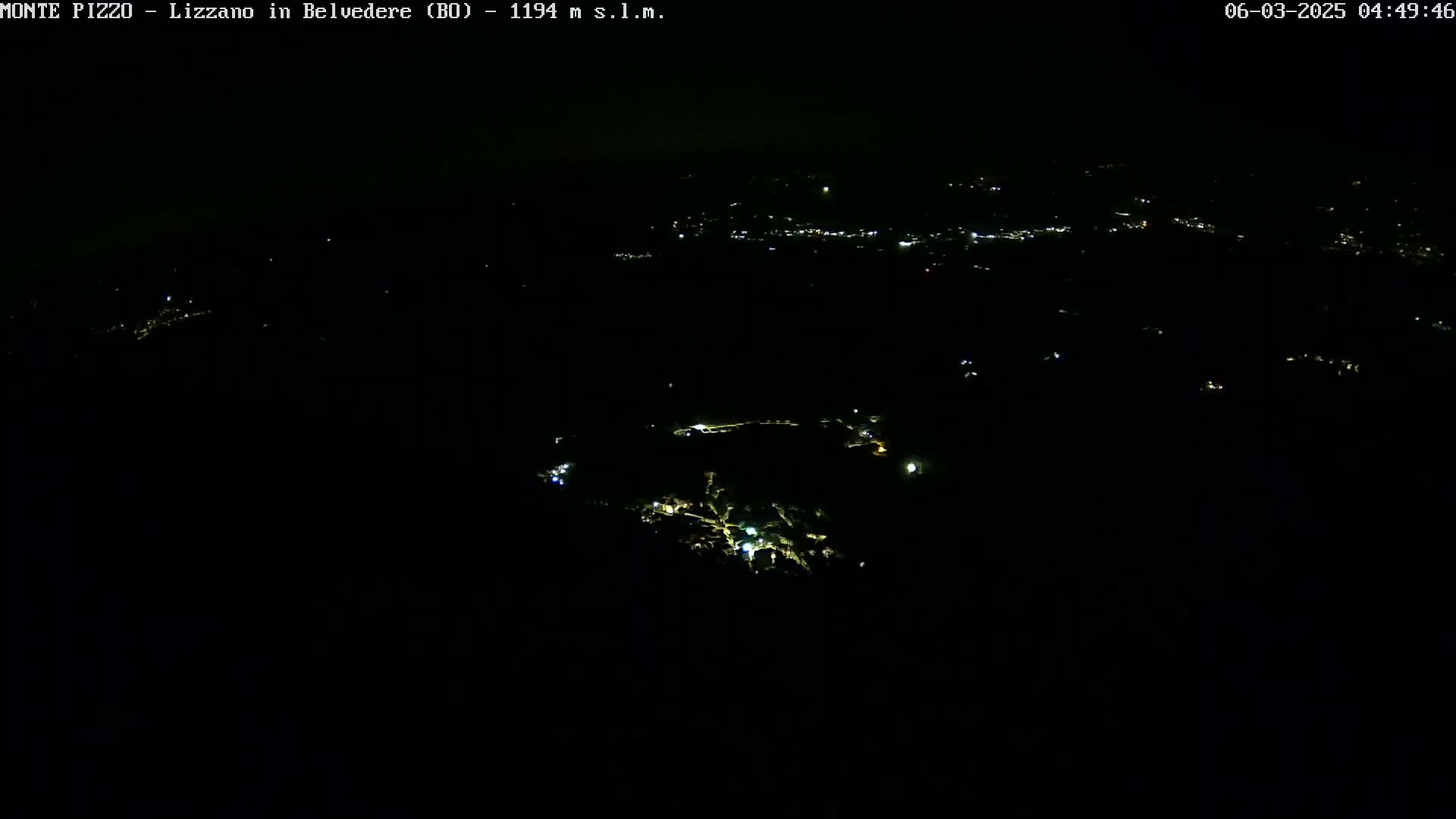 A nighttime, high-angle view shows a scattering of faint lights across a dark landscape.
