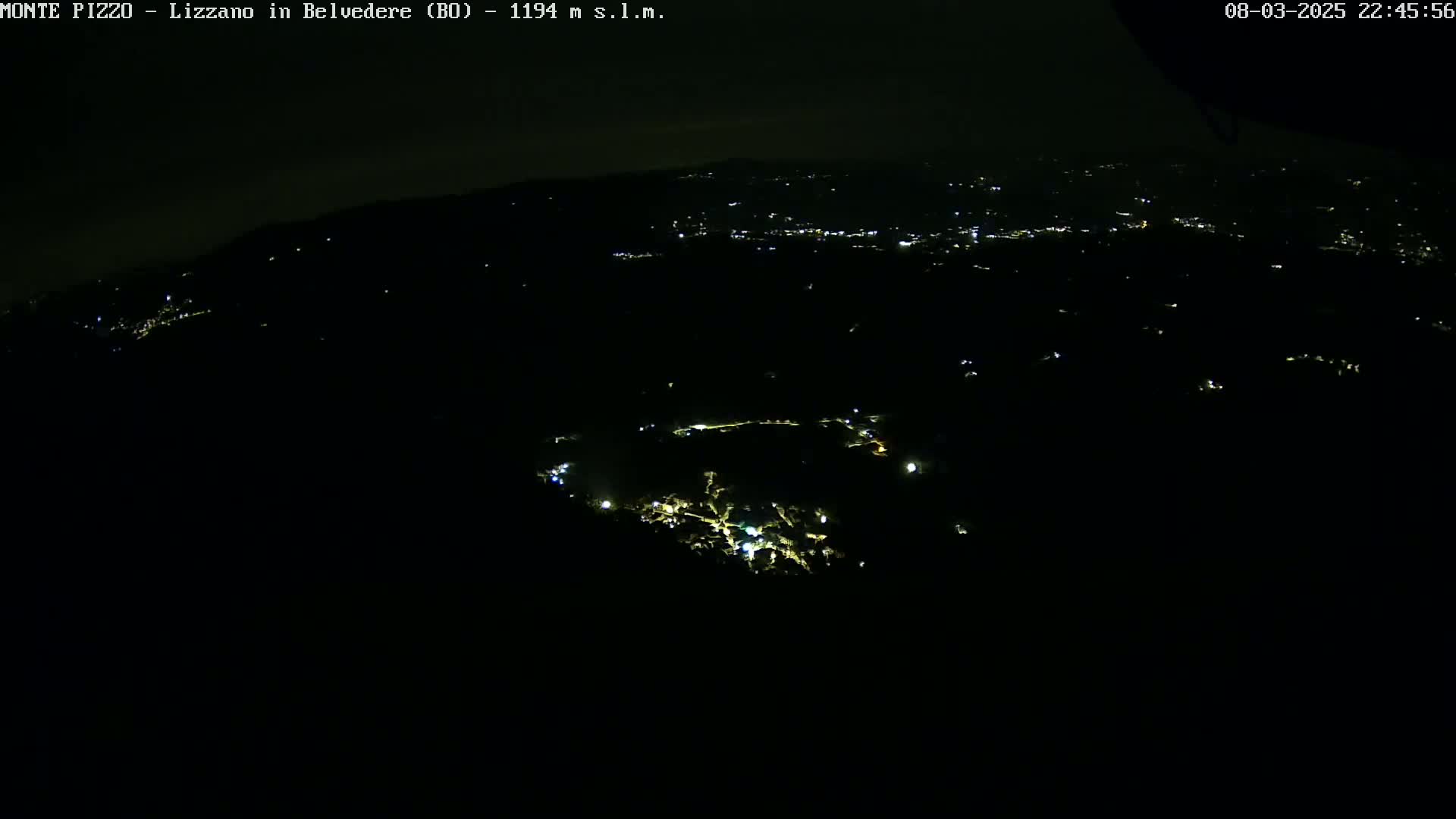 A nighttime, high-angle view shows a dark landscape sparsely dotted with small, distant lights.