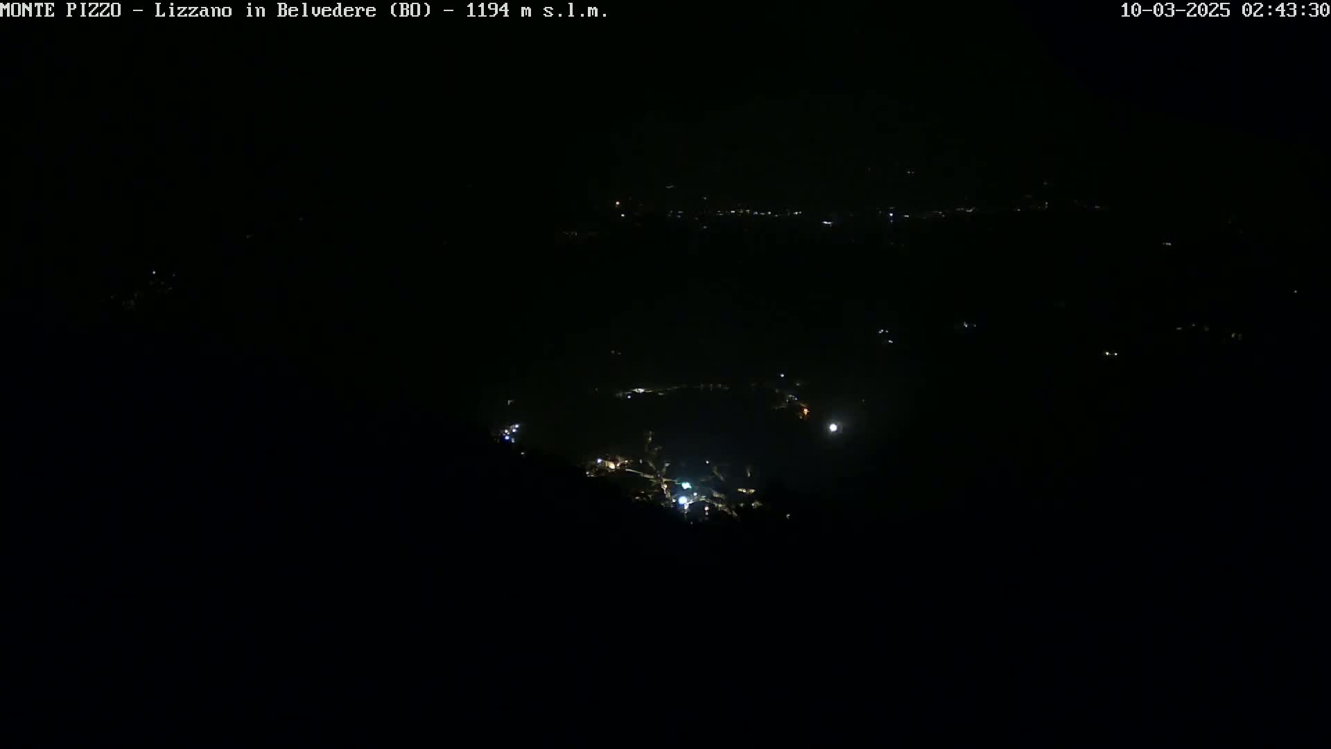 A nighttime, dark view of a distant town's scattered lights.