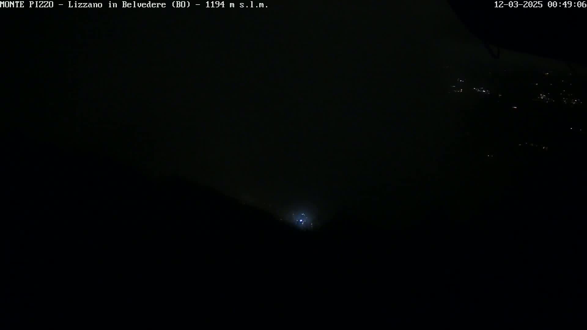 A nighttime, dark view shows a faint light source in the distance, possibly city lights, under a cloudy sky.