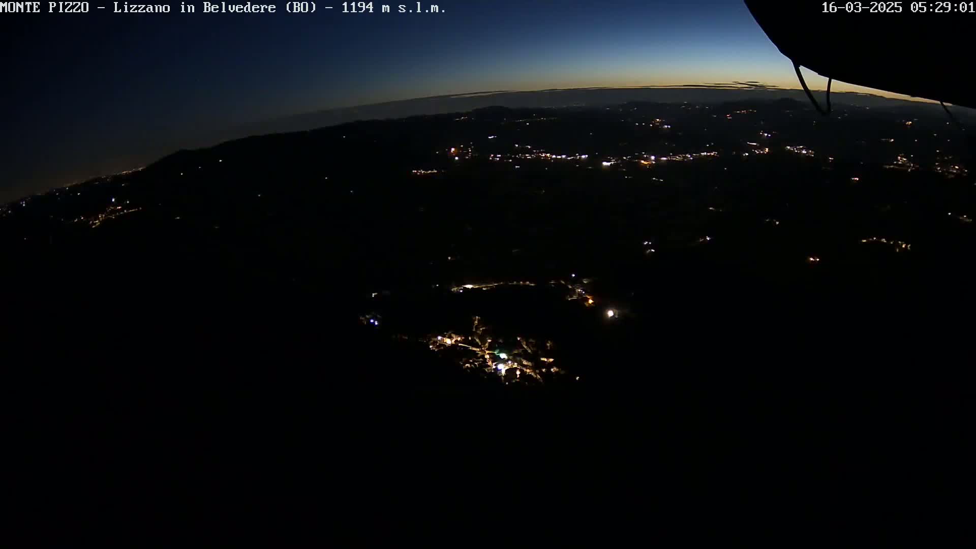 A nighttime aerial view shows a dark landscape with sparsely scattered lights below, under a twilight sky.