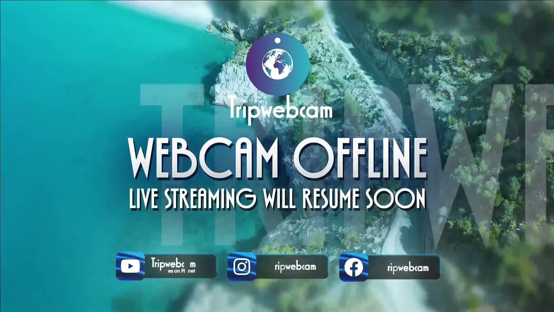 An aerial view of a coastline with turquoise water and green vegetation shows a webcam is temporarily offline.