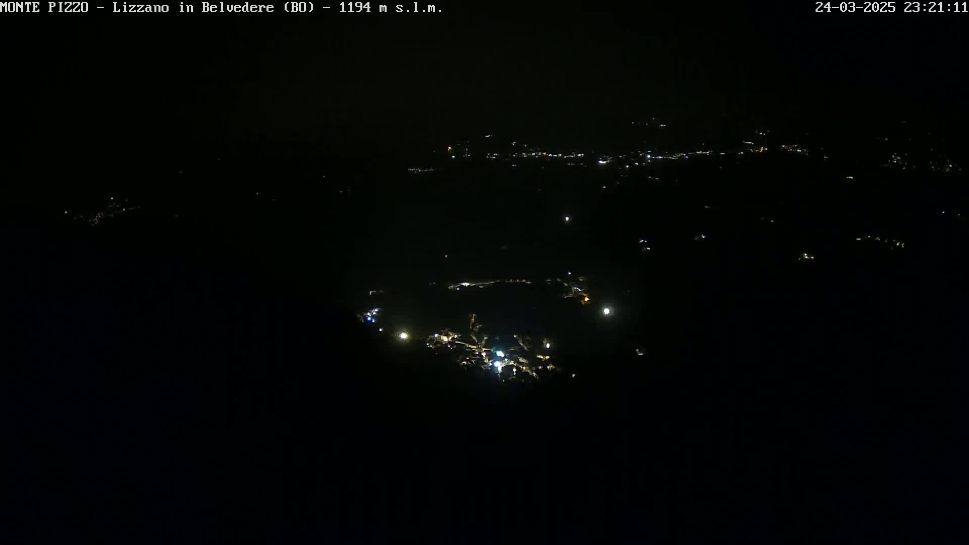A nighttime, high-angle view shows a scattering of small lights in the darkness, likely representing a town or village.