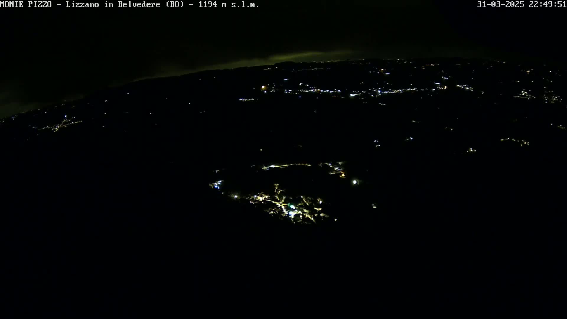 A nighttime aerial view shows a dark landscape with scattered lights from a town below.
