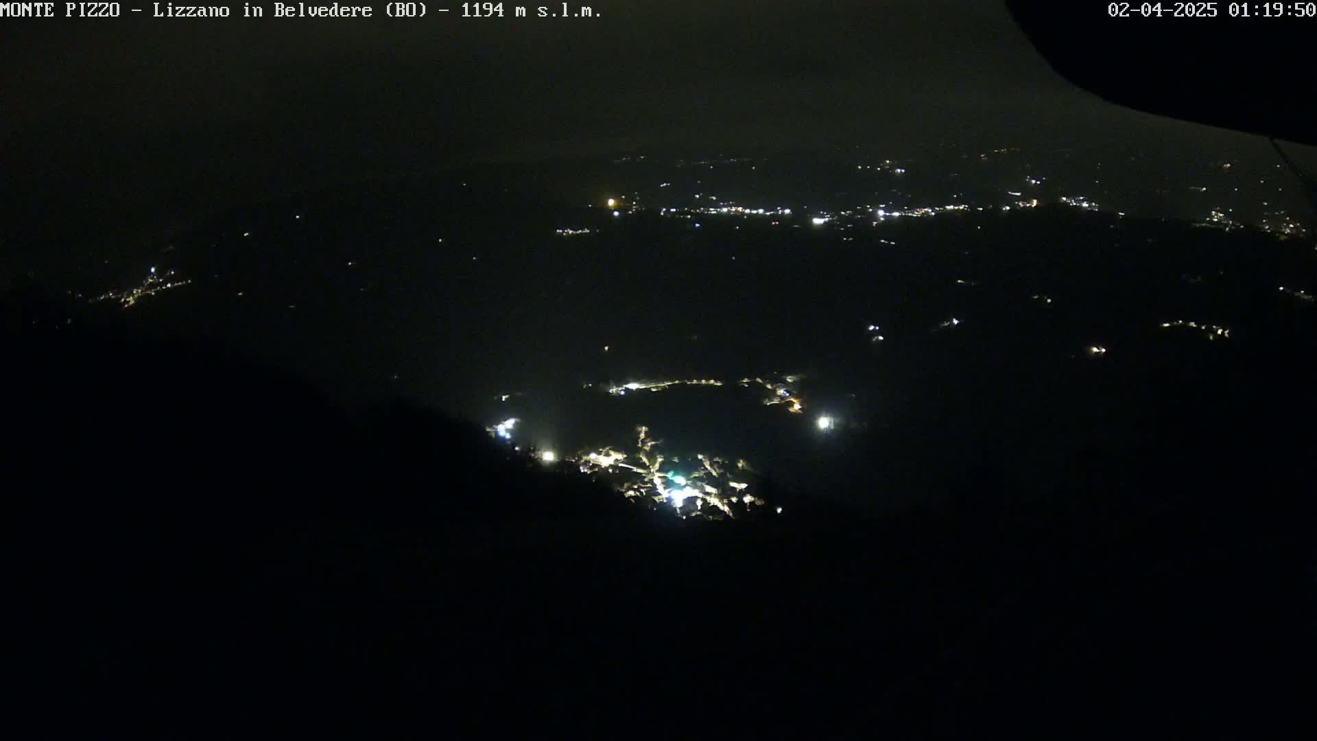 A nighttime, high-angle view shows a valley with scattered lights from a town or village below.