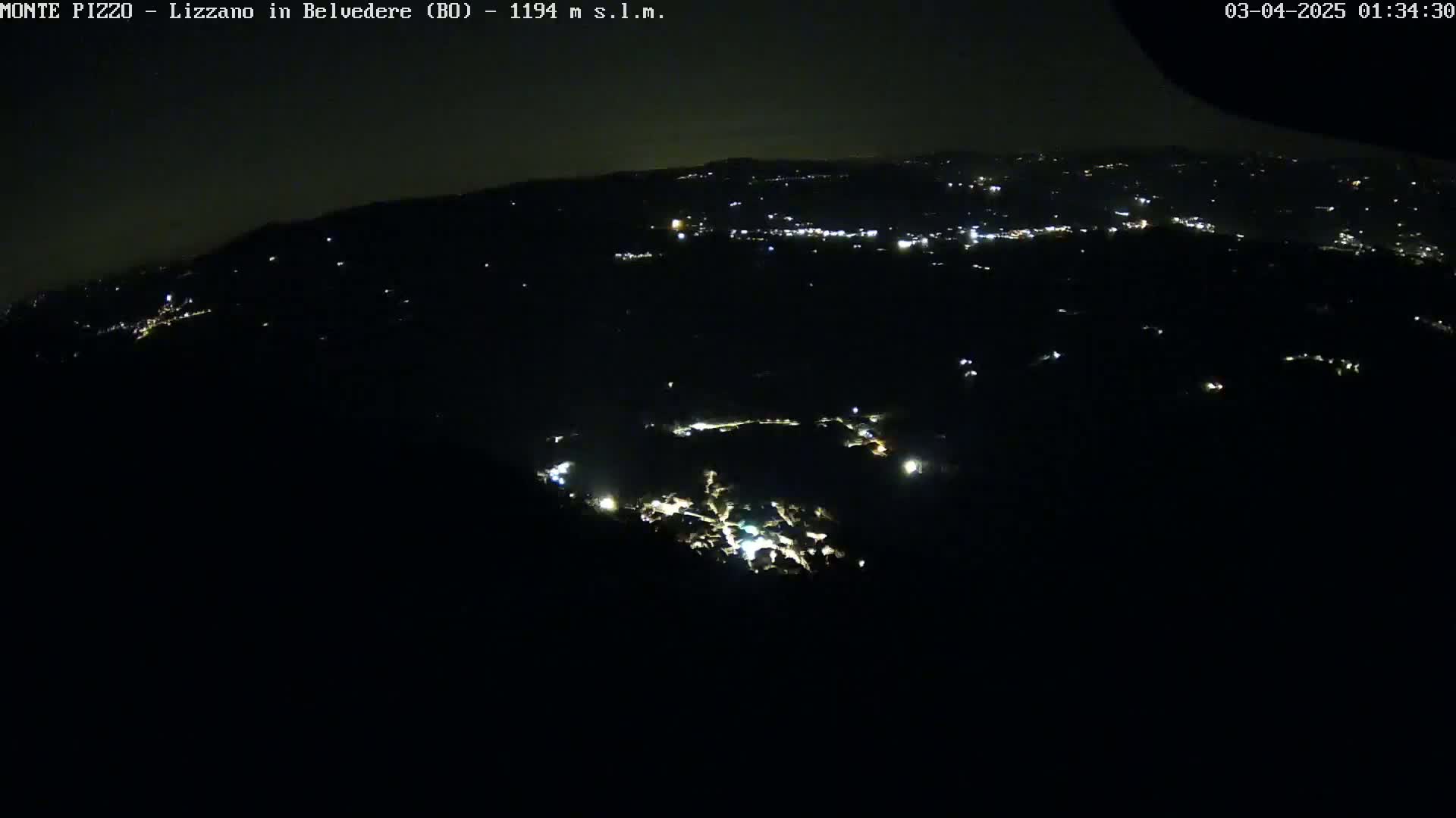 A nighttime, high-angle view shows a sprawling landscape with sparsely scattered lights illuminating a dark, hilly terrain.