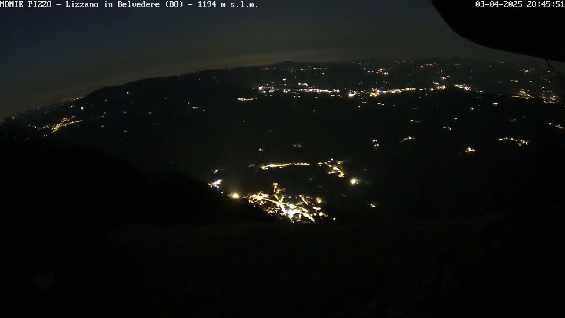 A nighttime aerial view shows a dark landscape speckled with the scattered lights of a town or village under a clear, dark sky.