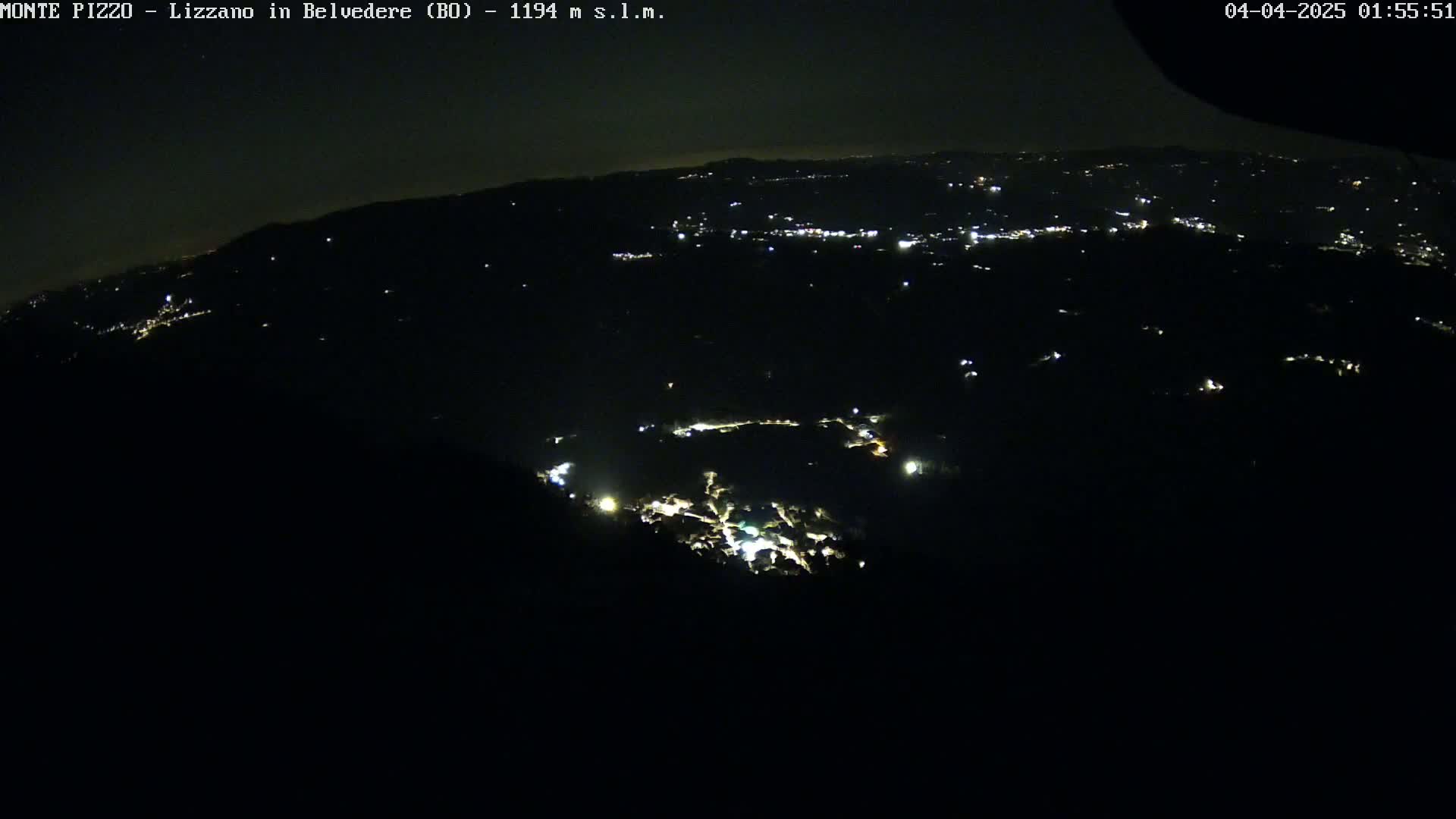 A nighttime, high-angle view shows a dark landscape speckled with scattered lights from a town or village below.