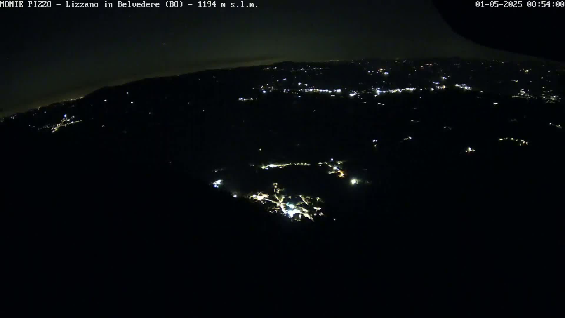 A nighttime, aerial view shows a sprawling town nestled in a dark landscape, illuminated by scattered lights.