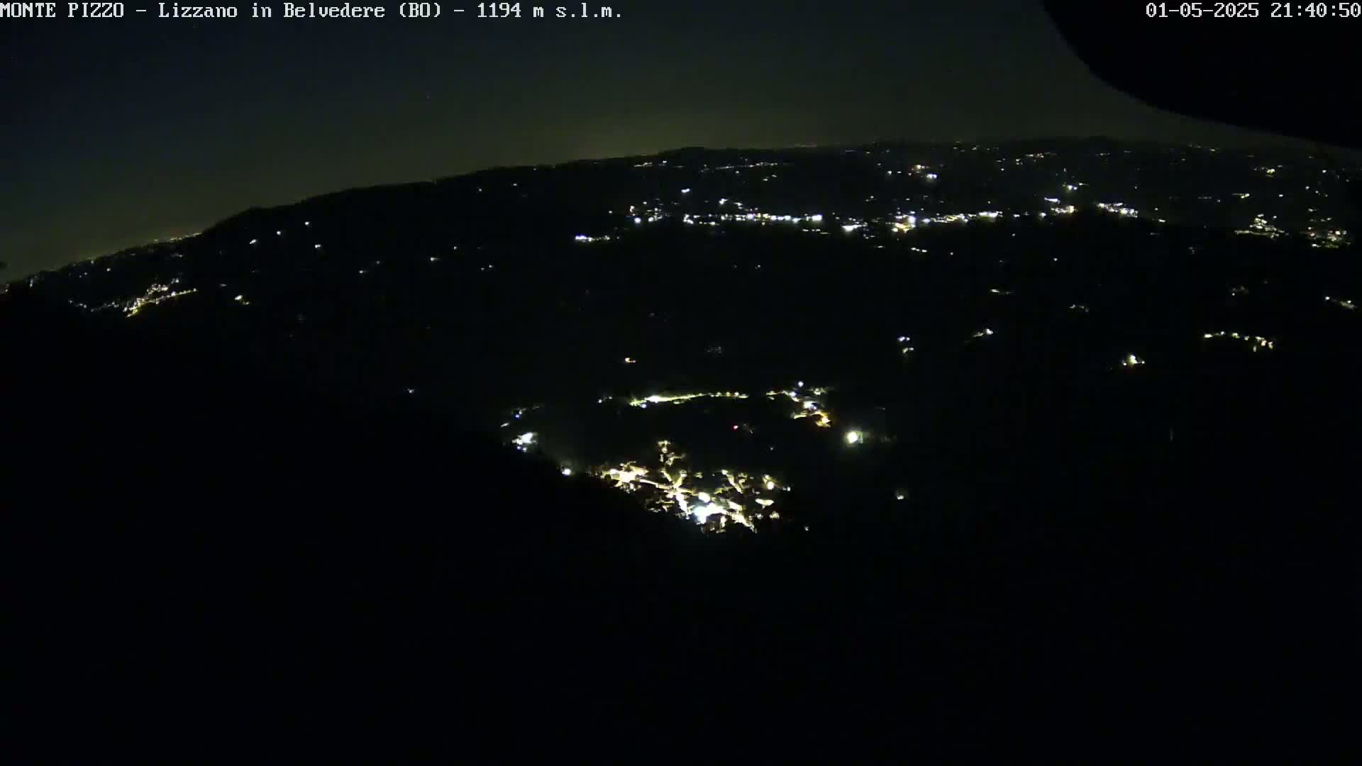 A nighttime, high-angle view shows a scattering of small, faint lights across a dark, hilly landscape.