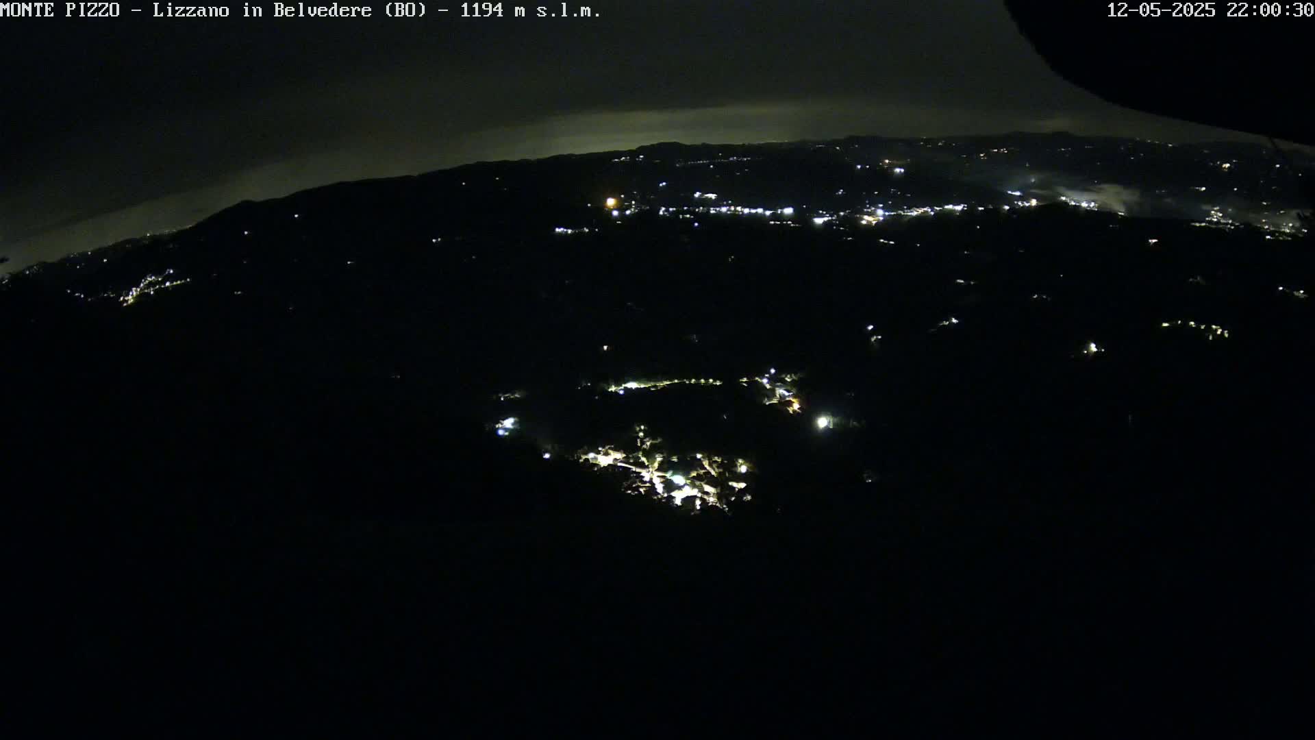A nighttime, high-angle view shows a dark landscape speckled with faint lights from a distant town, under a mostly clear sky.