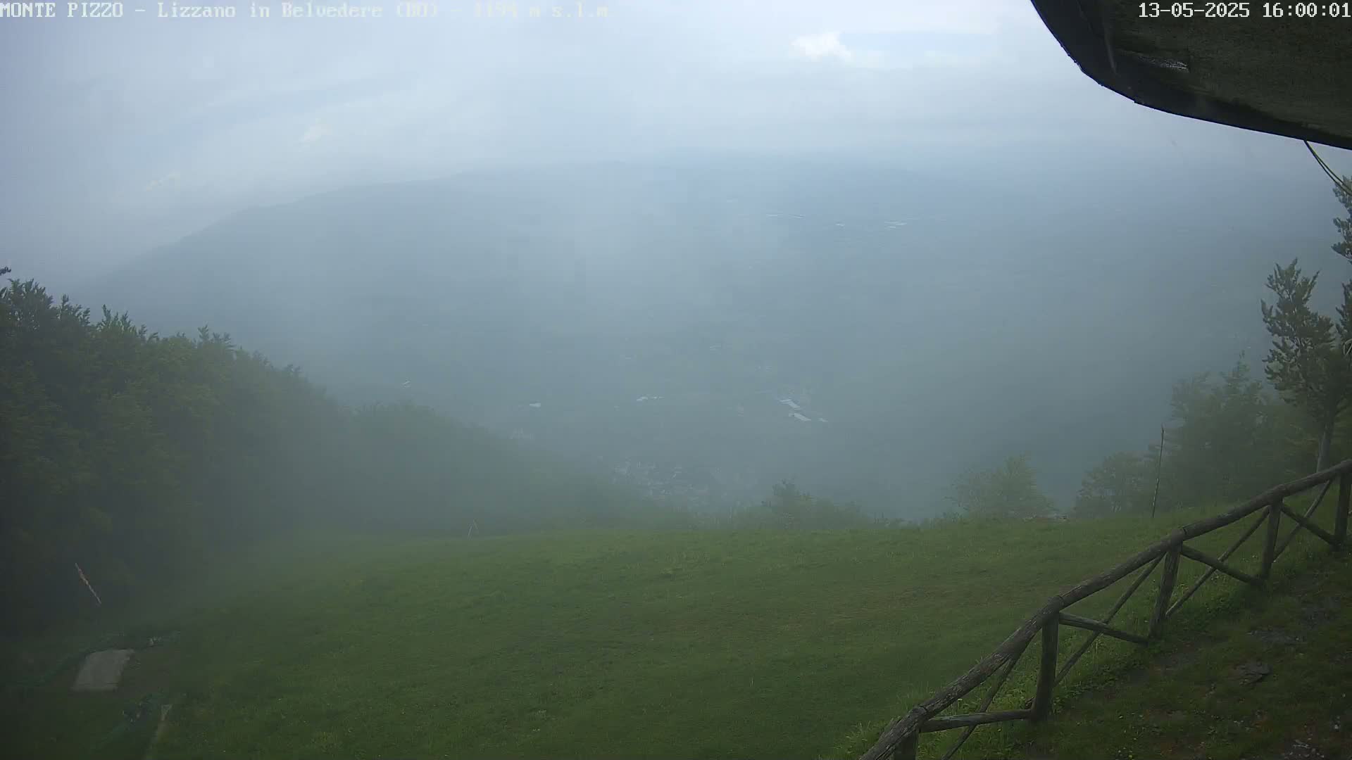 A foggy mountain vista reveals a distant valley and a grassy foreground with a wooden fence, partially obscured by mist.