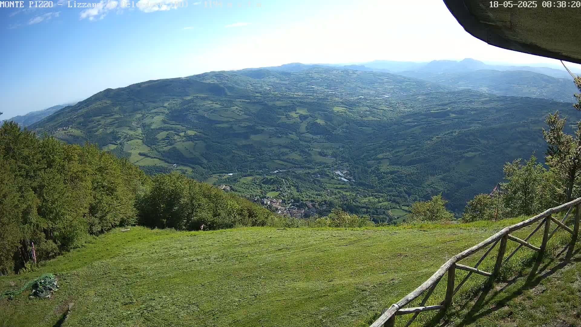 A grassy hilltop overlooks a vast, verdant valley under a clear sky.