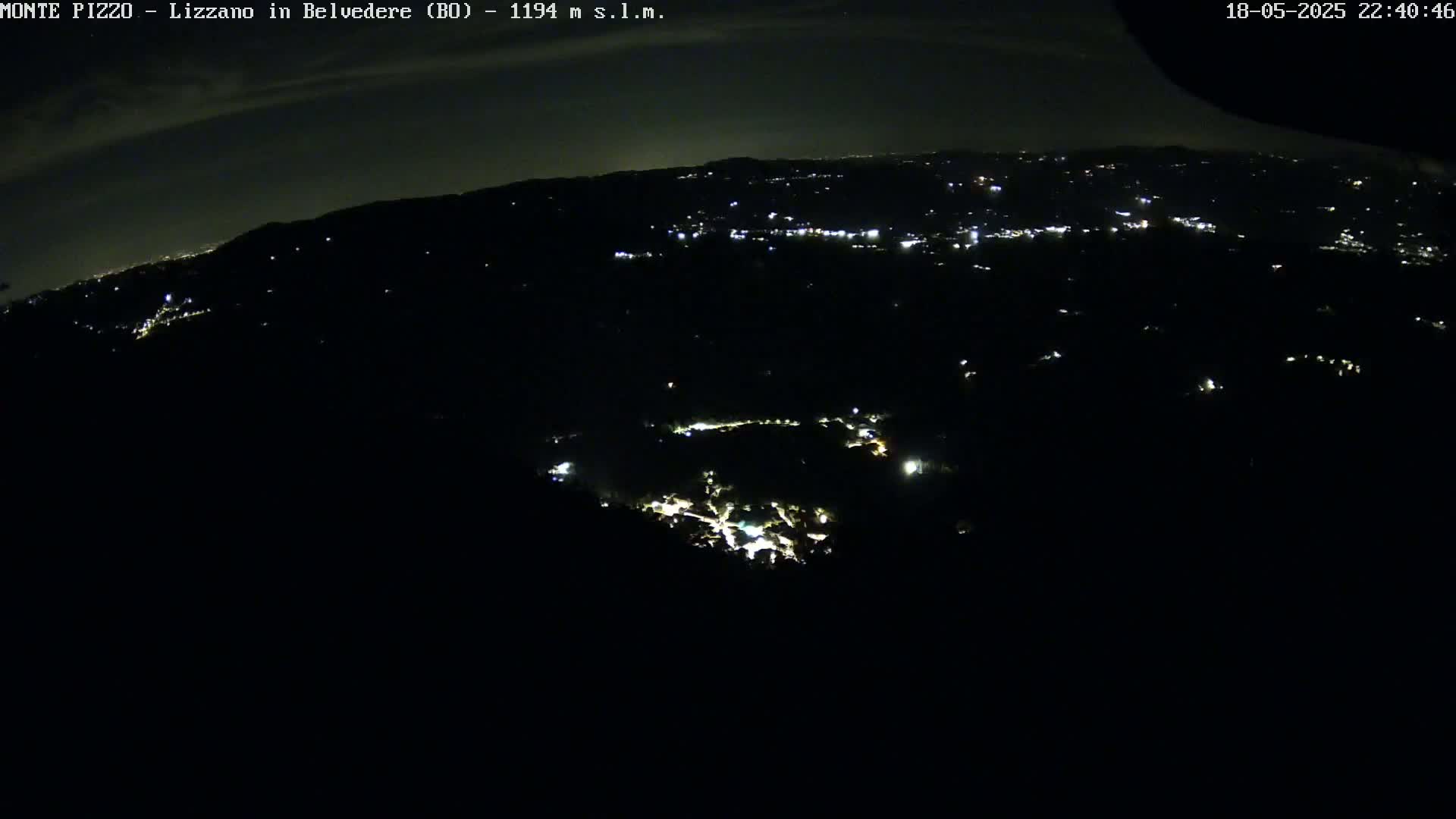 A nighttime, high-angle view shows a dark, hilly landscape speckled with small, distant lights.