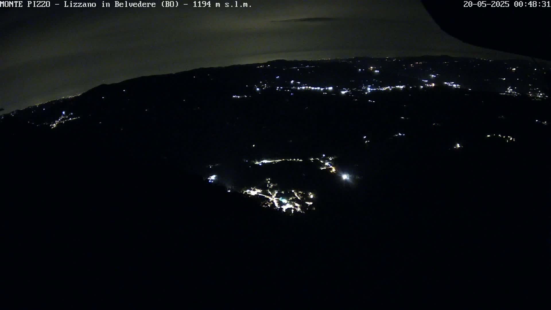 A nighttime, high-angle view shows a dark landscape speckled with small lights from a distant town.