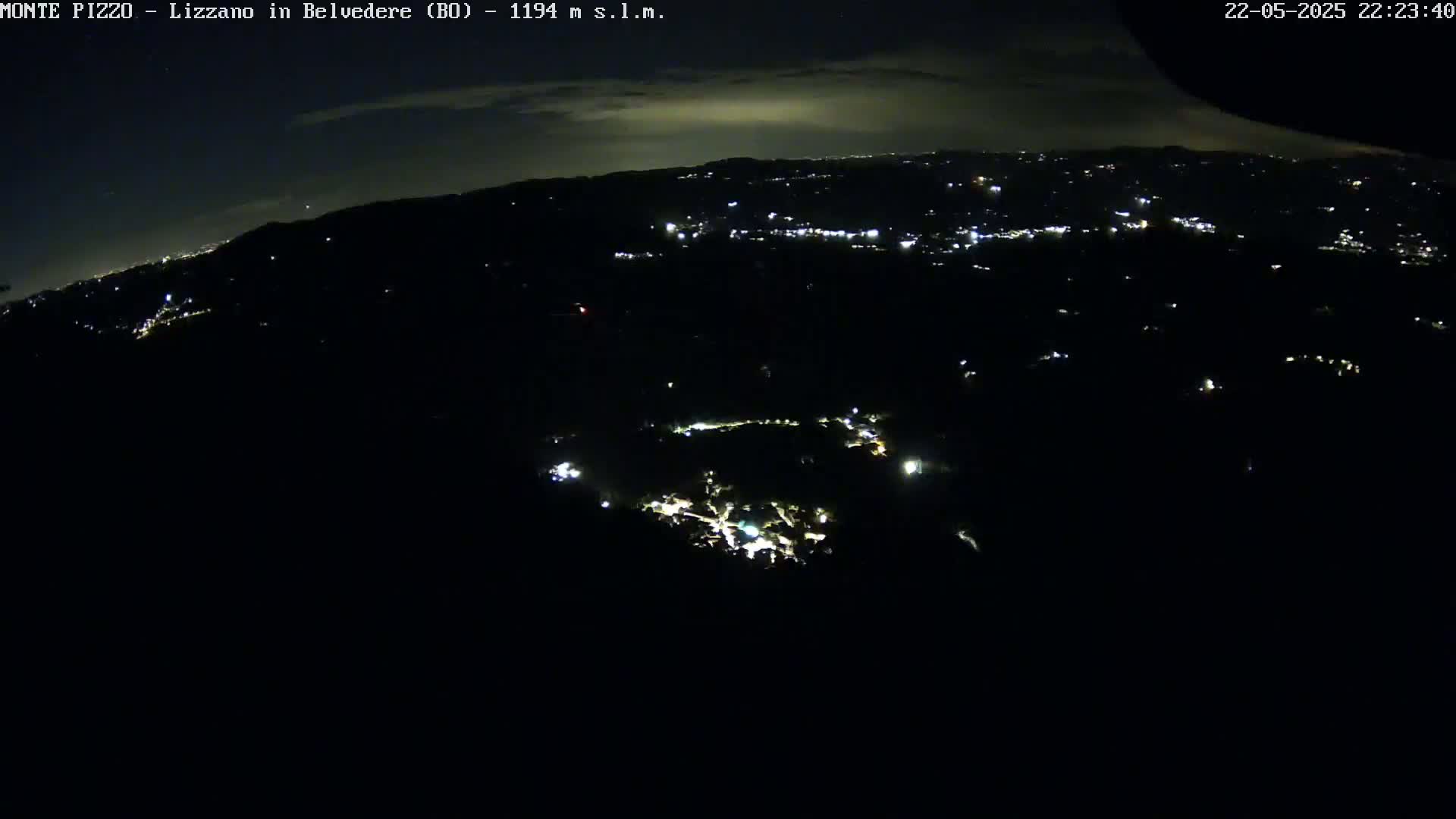 A nighttime aerial view shows a dark landscape speckled with the lights of a town below, under a mostly clear sky.