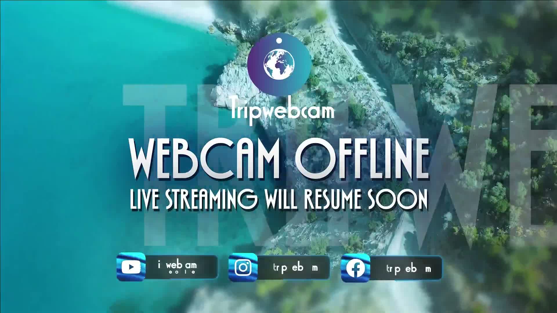 An aerial view of a rocky coastline and turquoise water is overlaid with a message indicating that the webcam is offline and live streaming will resume shortly.