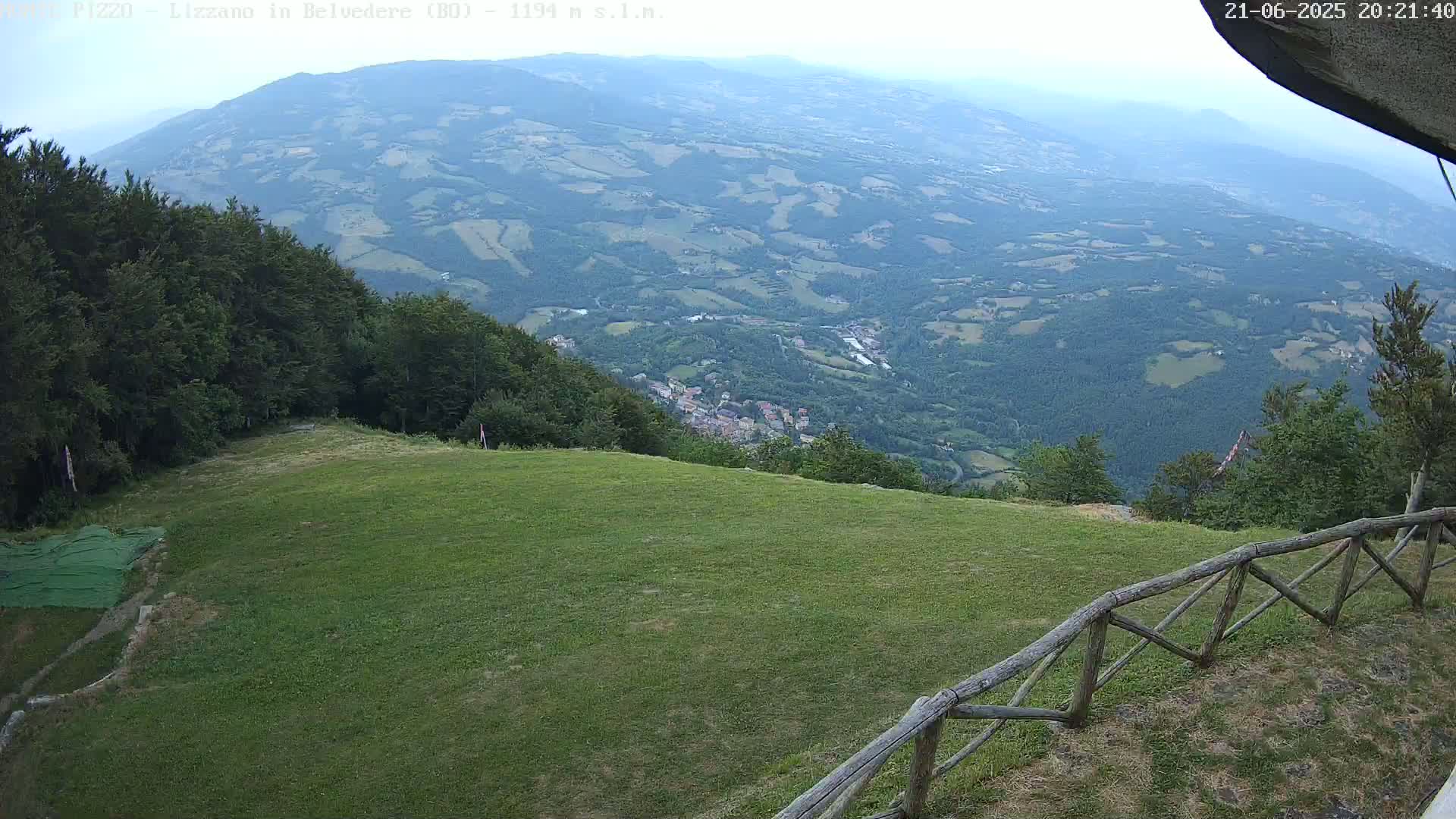 A grassy hilltop overlooks a valley of rolling hills and a town under an overcast sky.