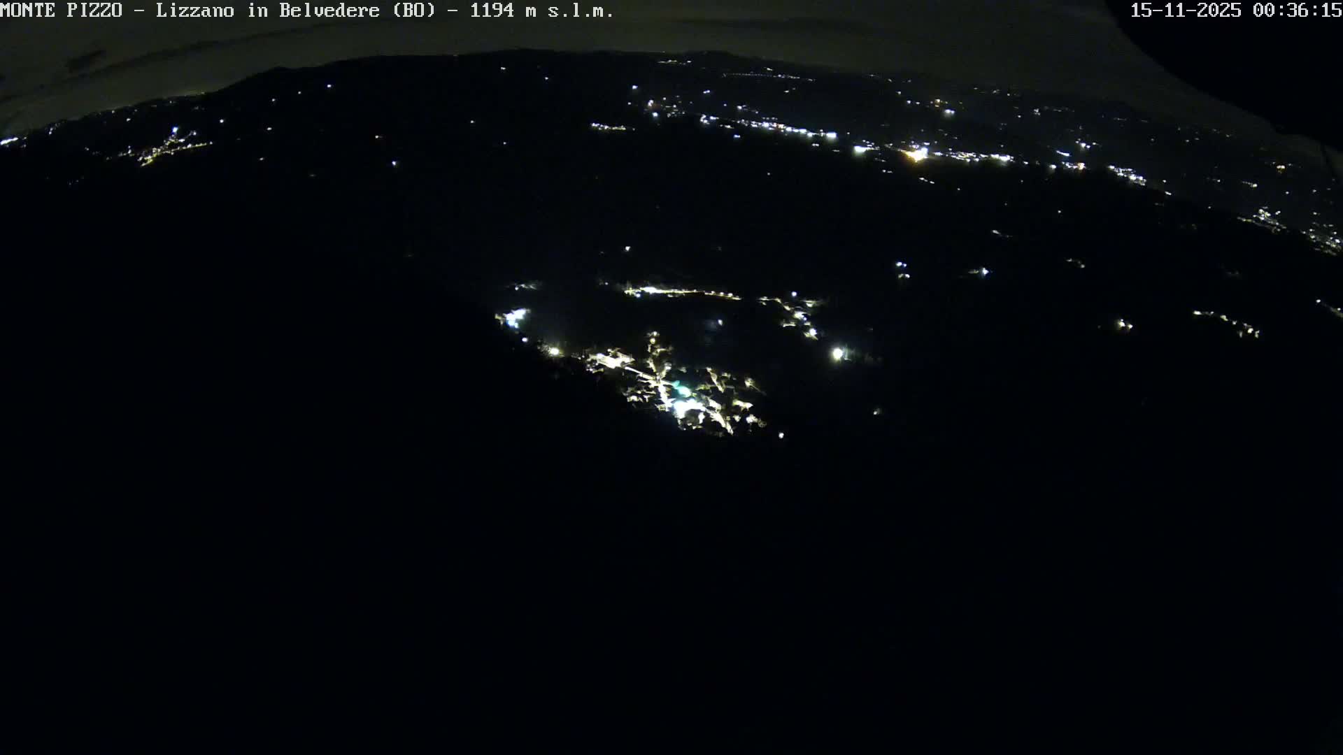 A clear night reveals a brightly lit town nestled in a valley, with scattered lights of other communities and roads extending across the dark, hilly landscape.