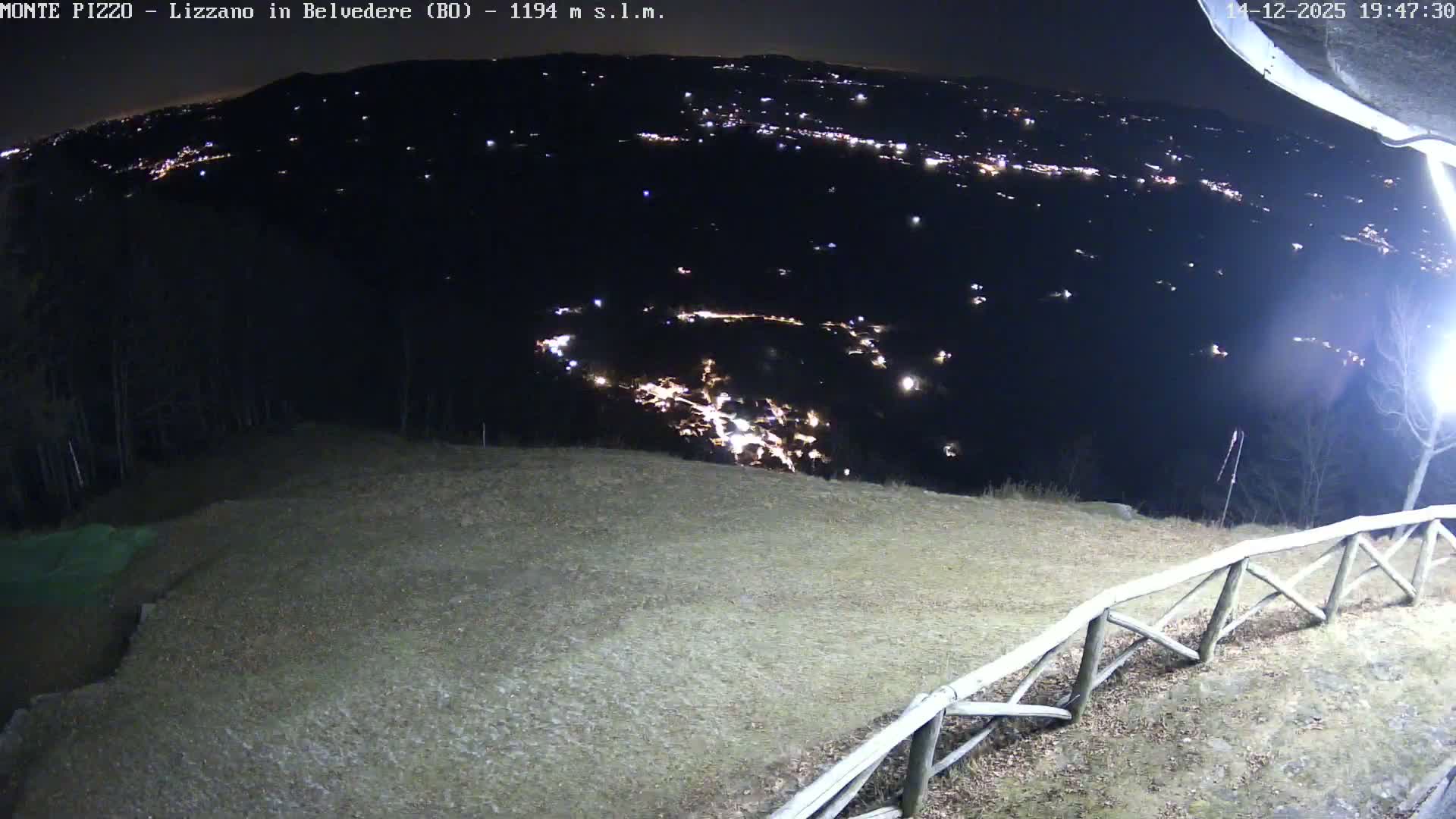 A foggy outdoor landscape features a grassy hillside with a rustic wooden fence in the foreground, while distant bare trees and mountains are heavily obscured by dense mist, resulting in very low visibility.