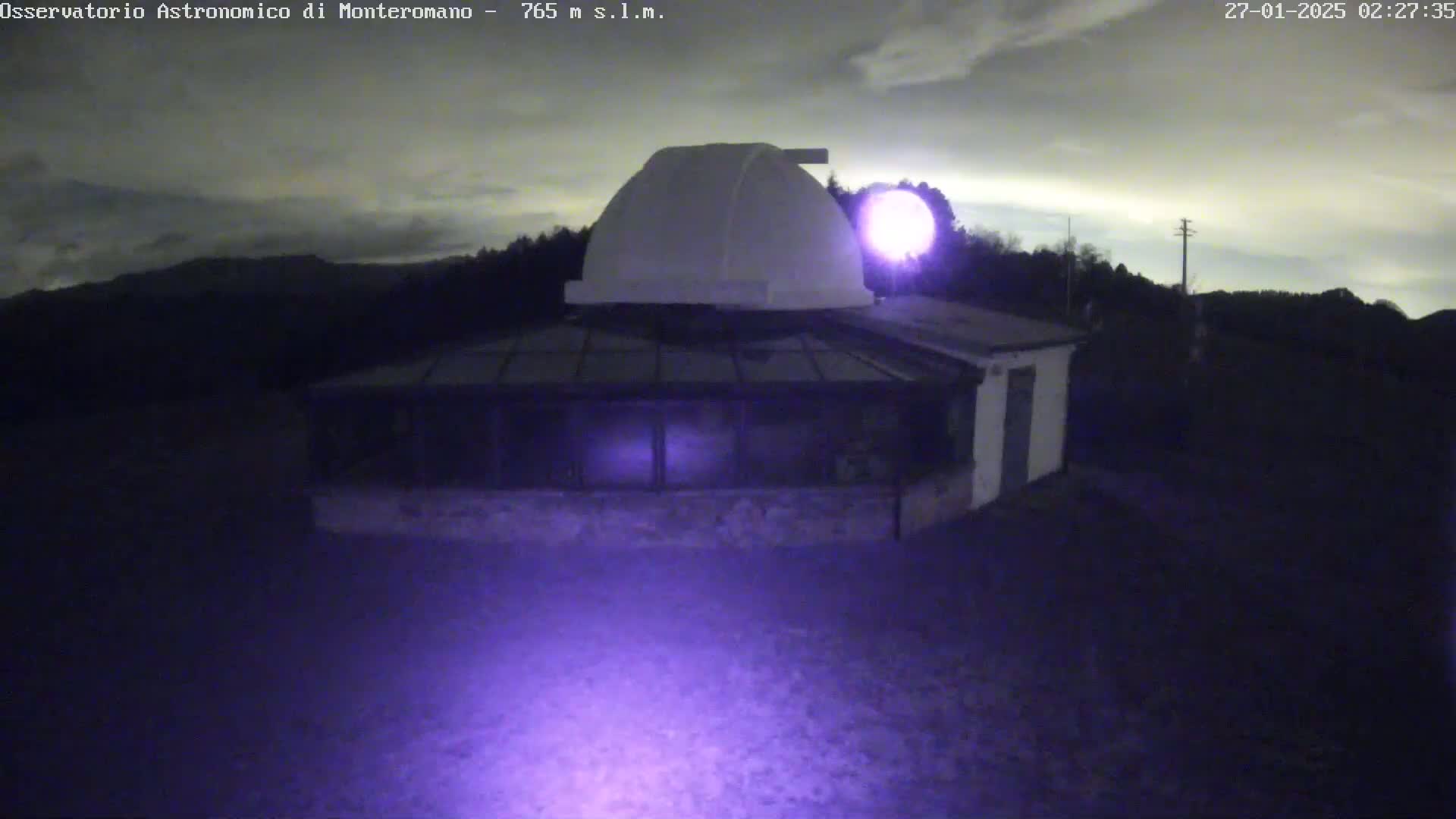 At night, under a cloudy sky, a low-lying observatory building with a dome sits on a dark, empty grounds.
