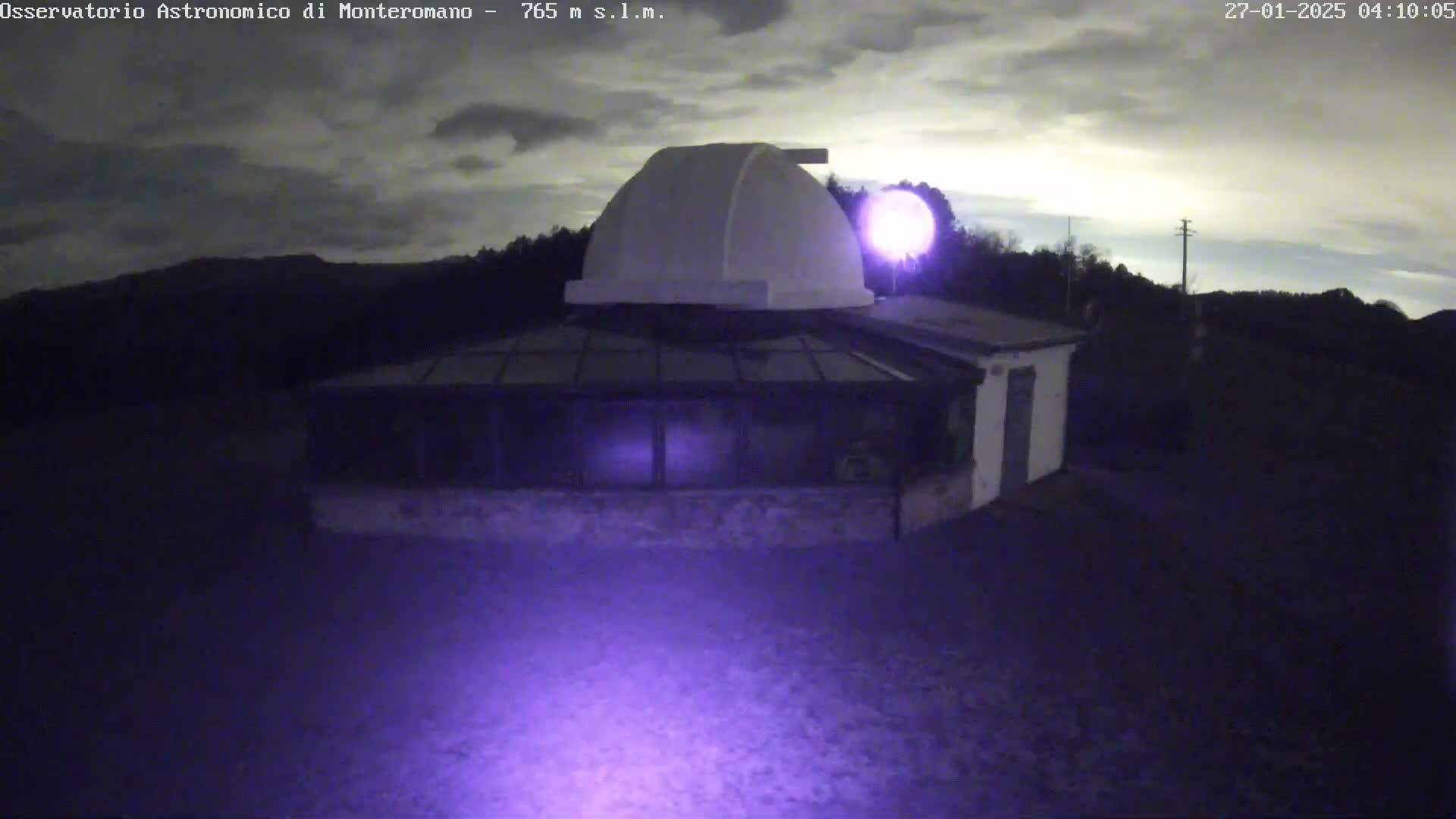 Here is a description of the image: An observatory building with a dome sits under a partly cloudy night sky.