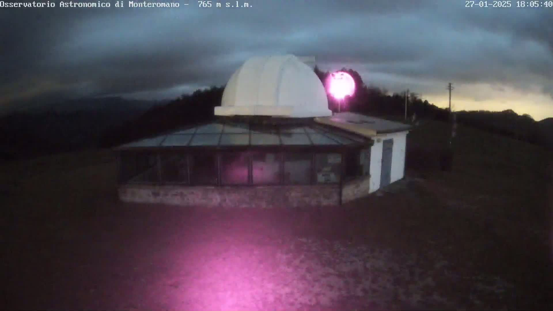 An observatory building with a dome sits on a hill under a cloudy twilight sky.