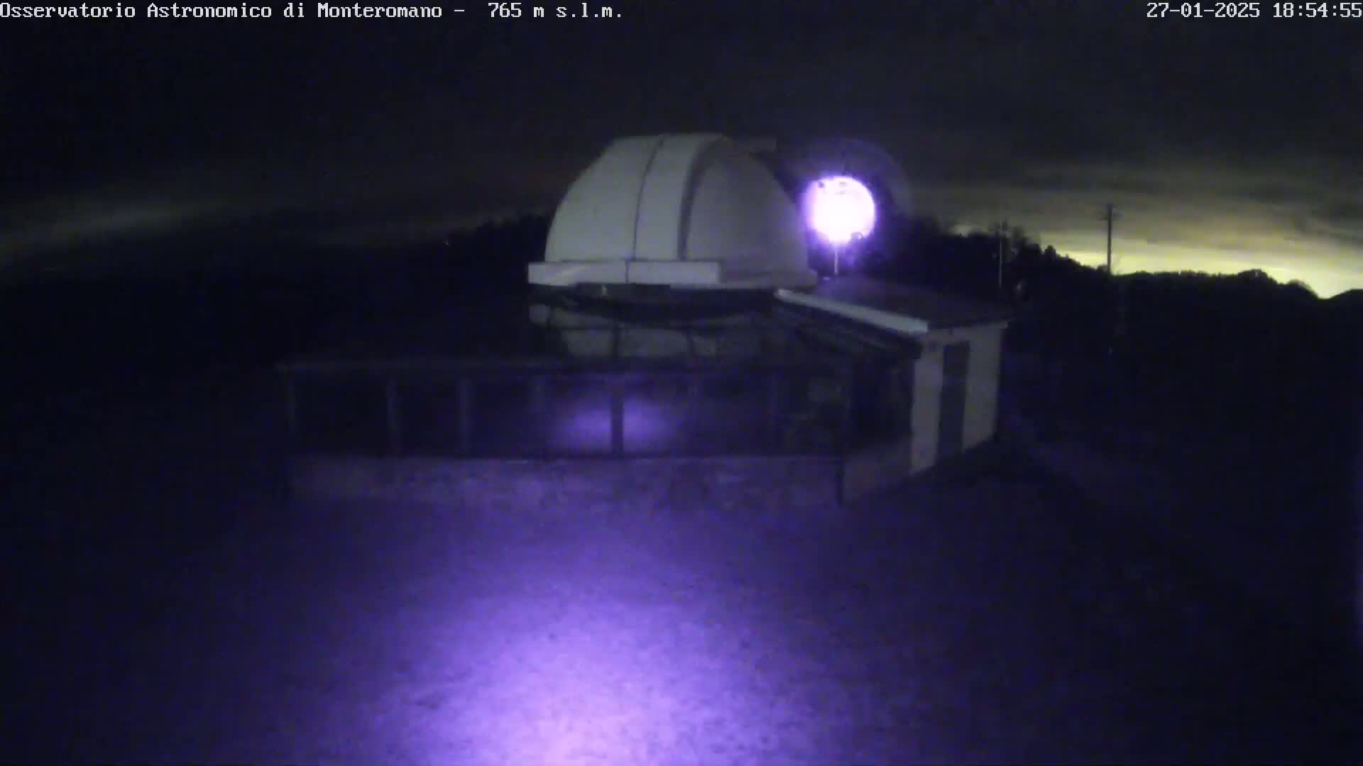 A nighttime view of an observatory building with a dome under a mostly clear sky.
