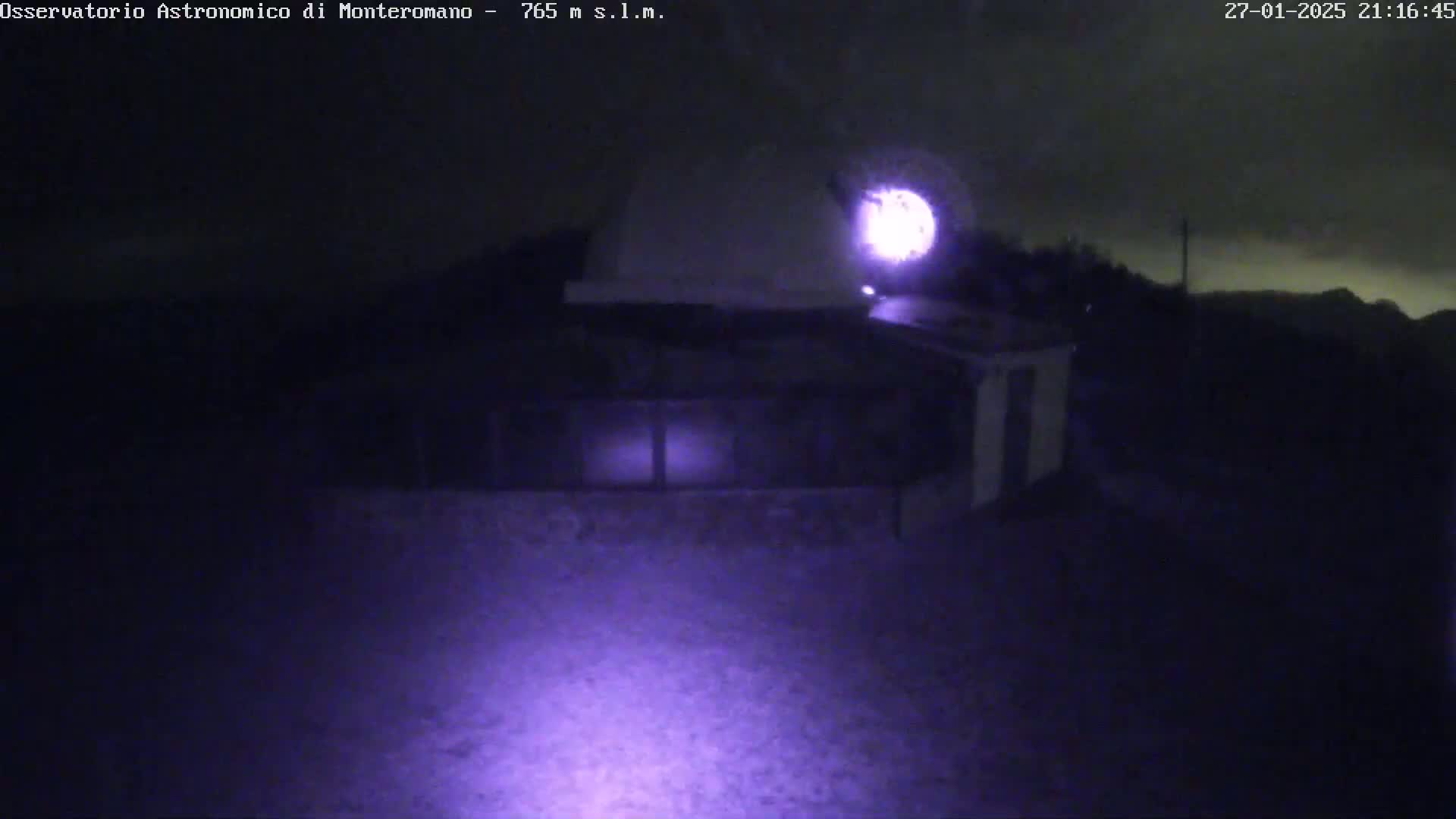 A nighttime, low-light view shows a building with a dome, possibly an observatory, under a dark, possibly cloudy sky.