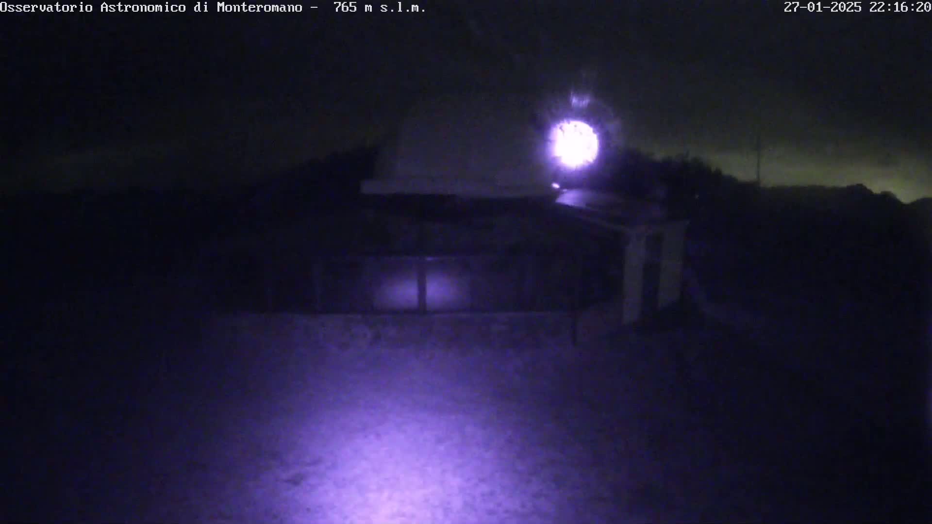 A nighttime, low-light image shows a building with a bright light source above it and a dim, possibly snowy, ground in front.