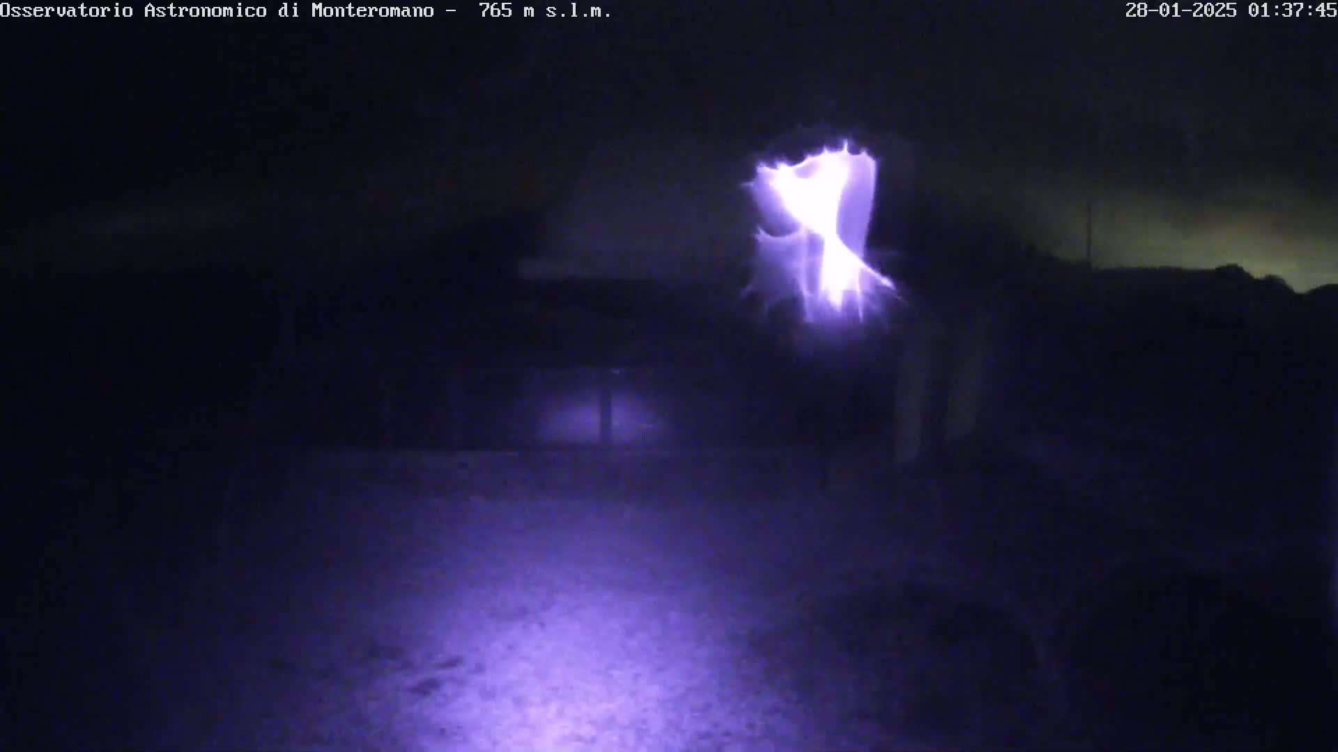 A bright purple light, possibly lightning, illuminates a dark, nighttime outdoor scene.