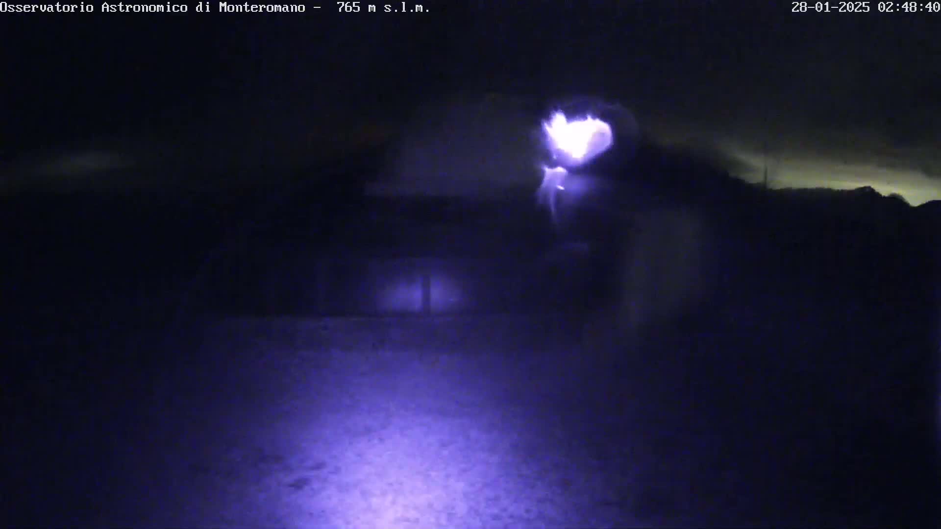 A nighttime, low-light view shows a bright light source in the center, possibly a flashlight, illuminating a dark, mostly featureless outdoor area.