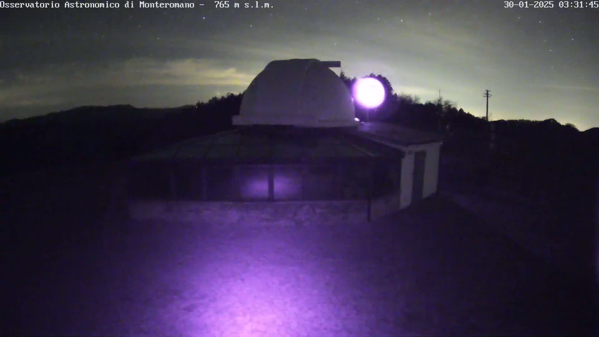 A low-light nighttime image shows an observatory building with a dome, situated on a hill under a mostly clear, starry sky.