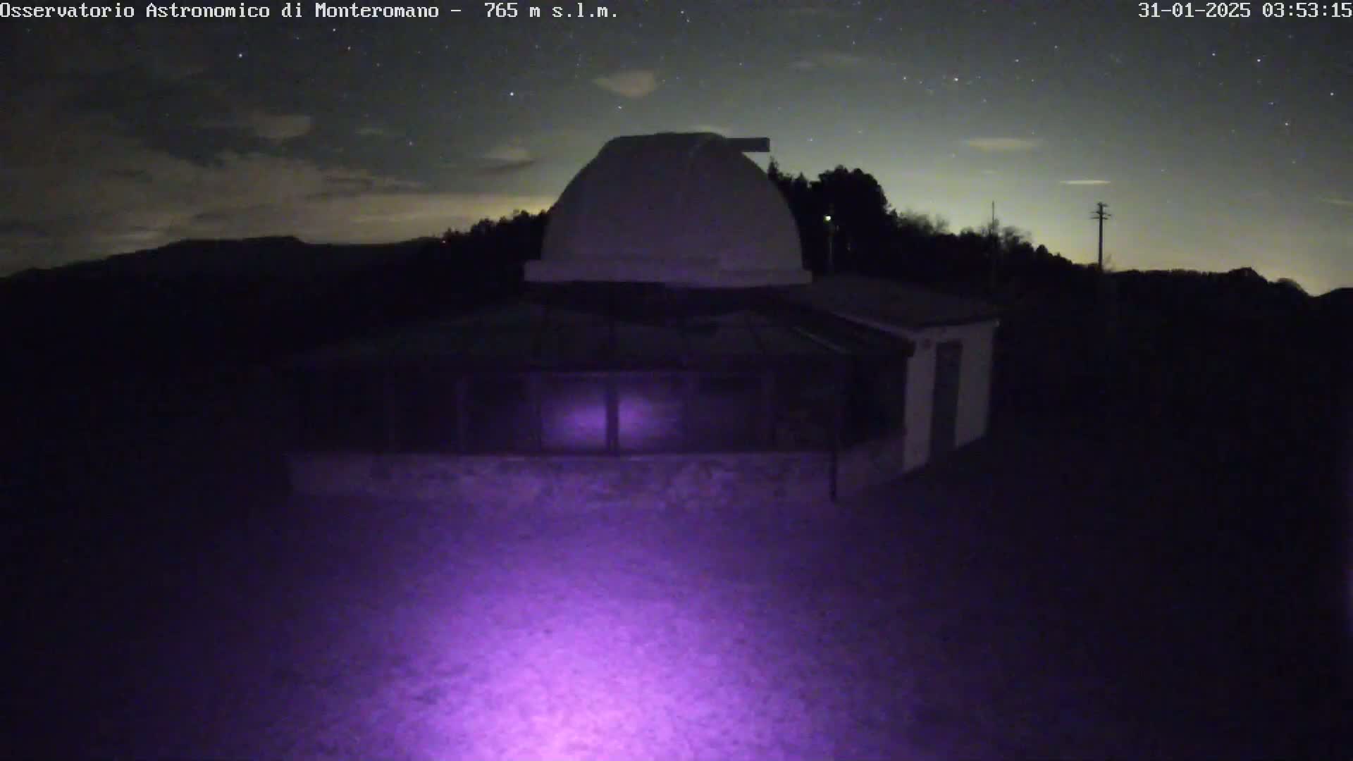A nighttime image shows a white observatory dome atop a low building under a partly cloudy, starry sky.