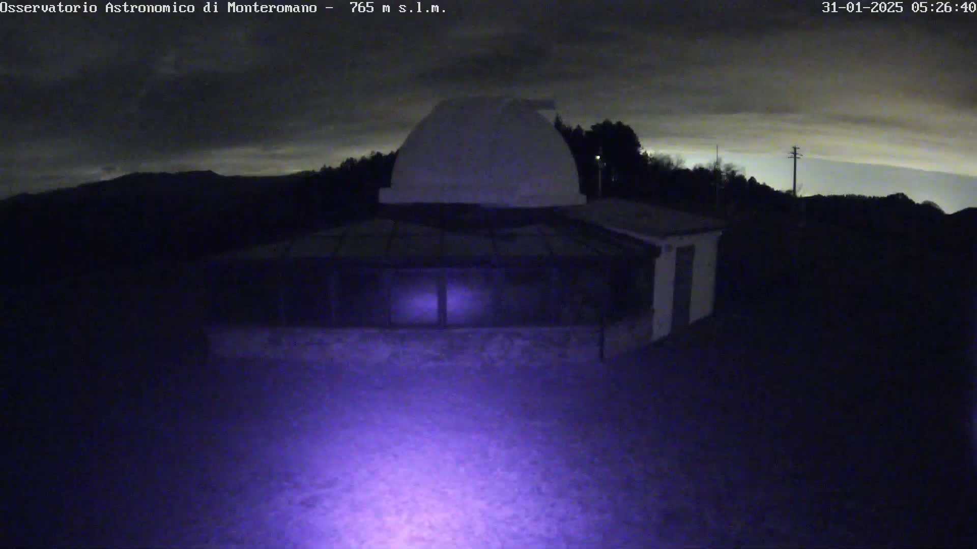 A nighttime view of a low-lying building with a dome on top, under a mostly cloudy sky.