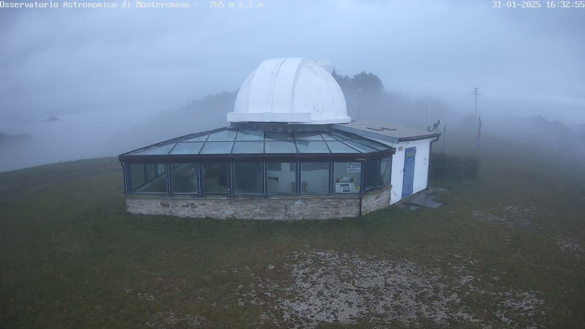A stone observatory building with a glass enclosure and a white dome sits on a grassy hill shrouded in fog.